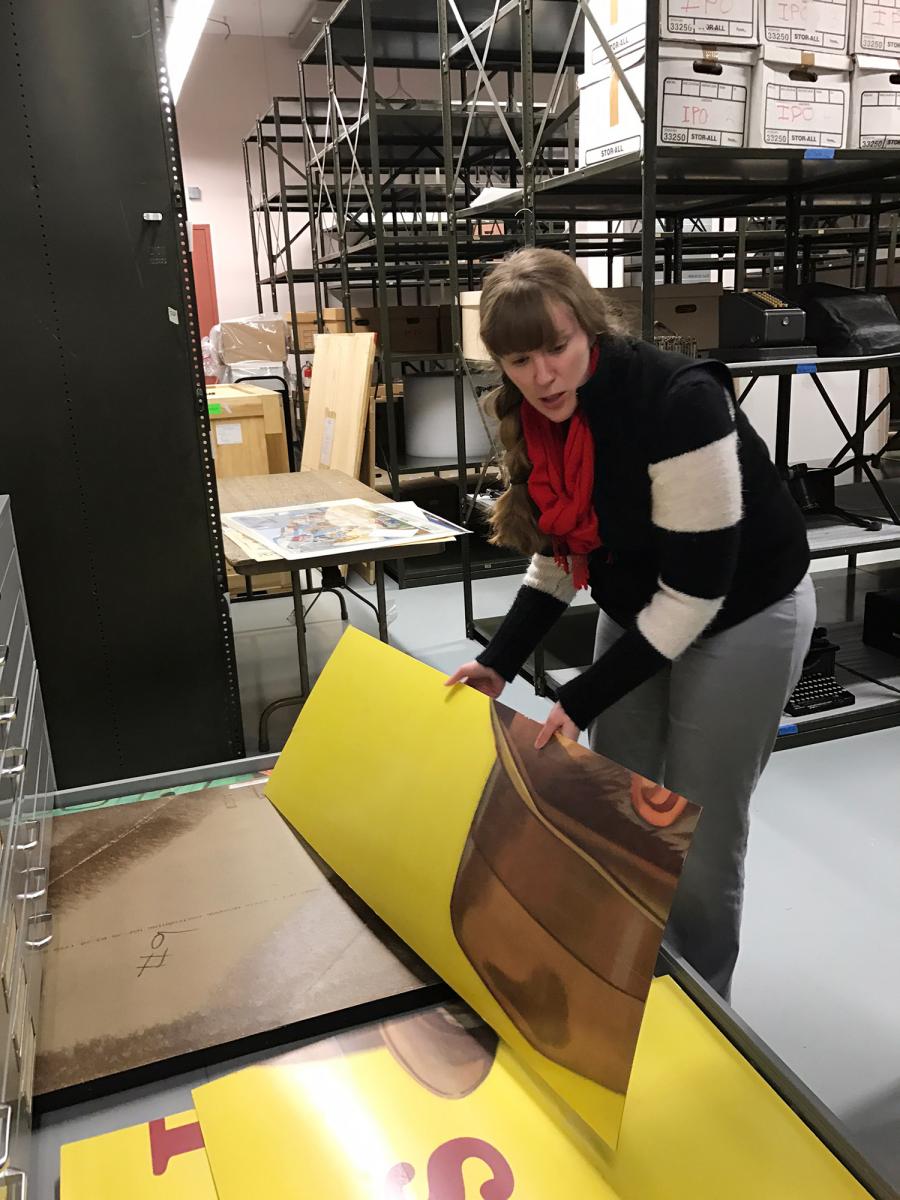 An archivist handles a piece of the large billboard stored in drawers in the archives.