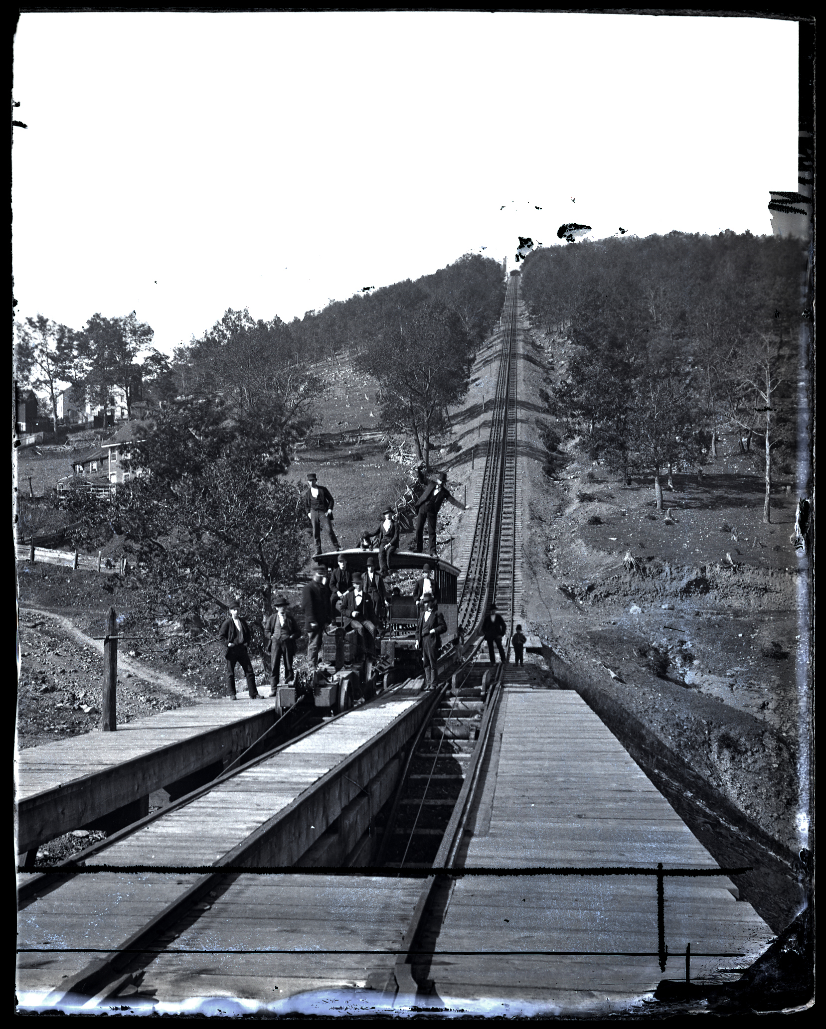 lack and white a image of a railcar at the base of a steep incline, with people aboard and nearby.