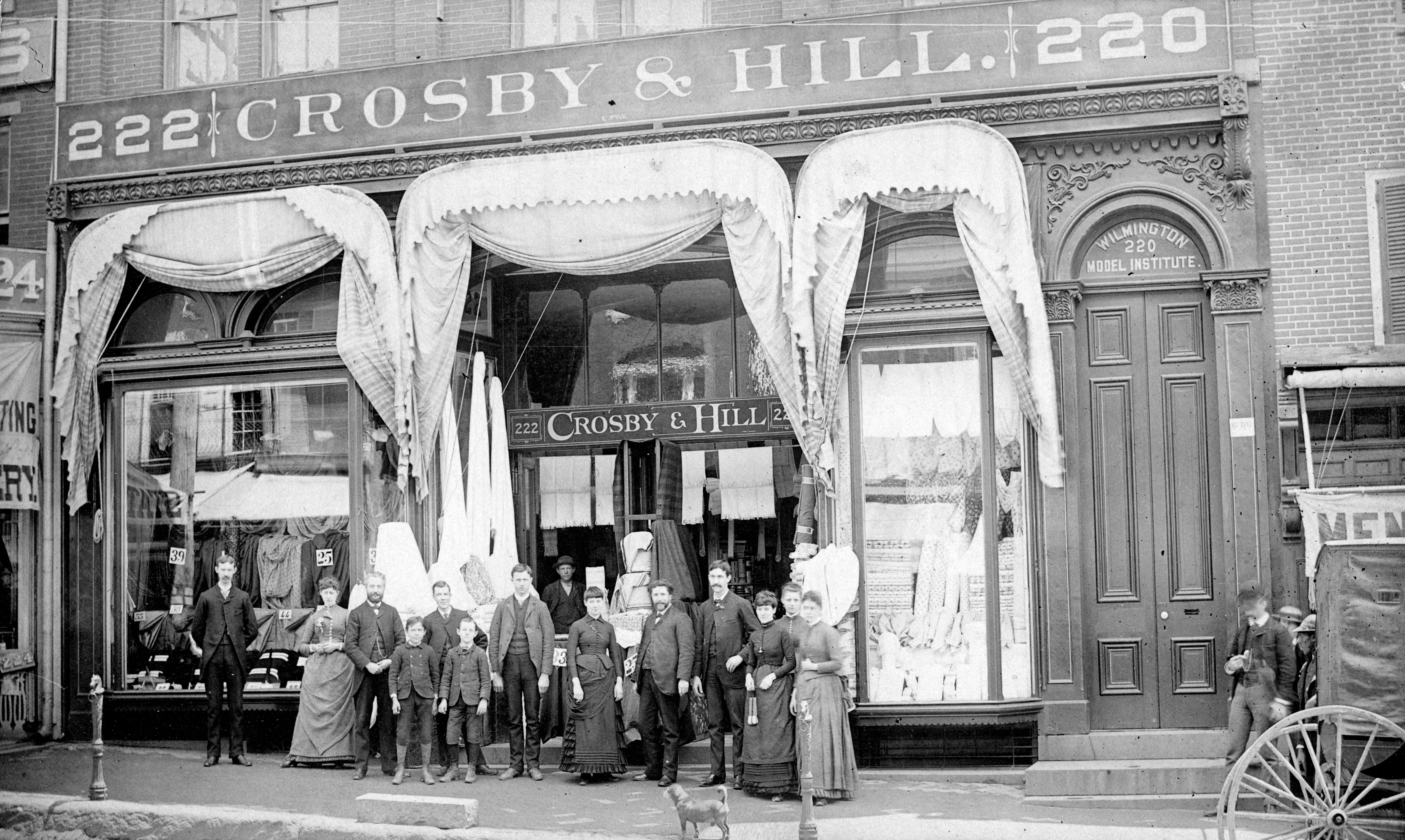 Black and white group photo of men, women, and children in front of a department store.