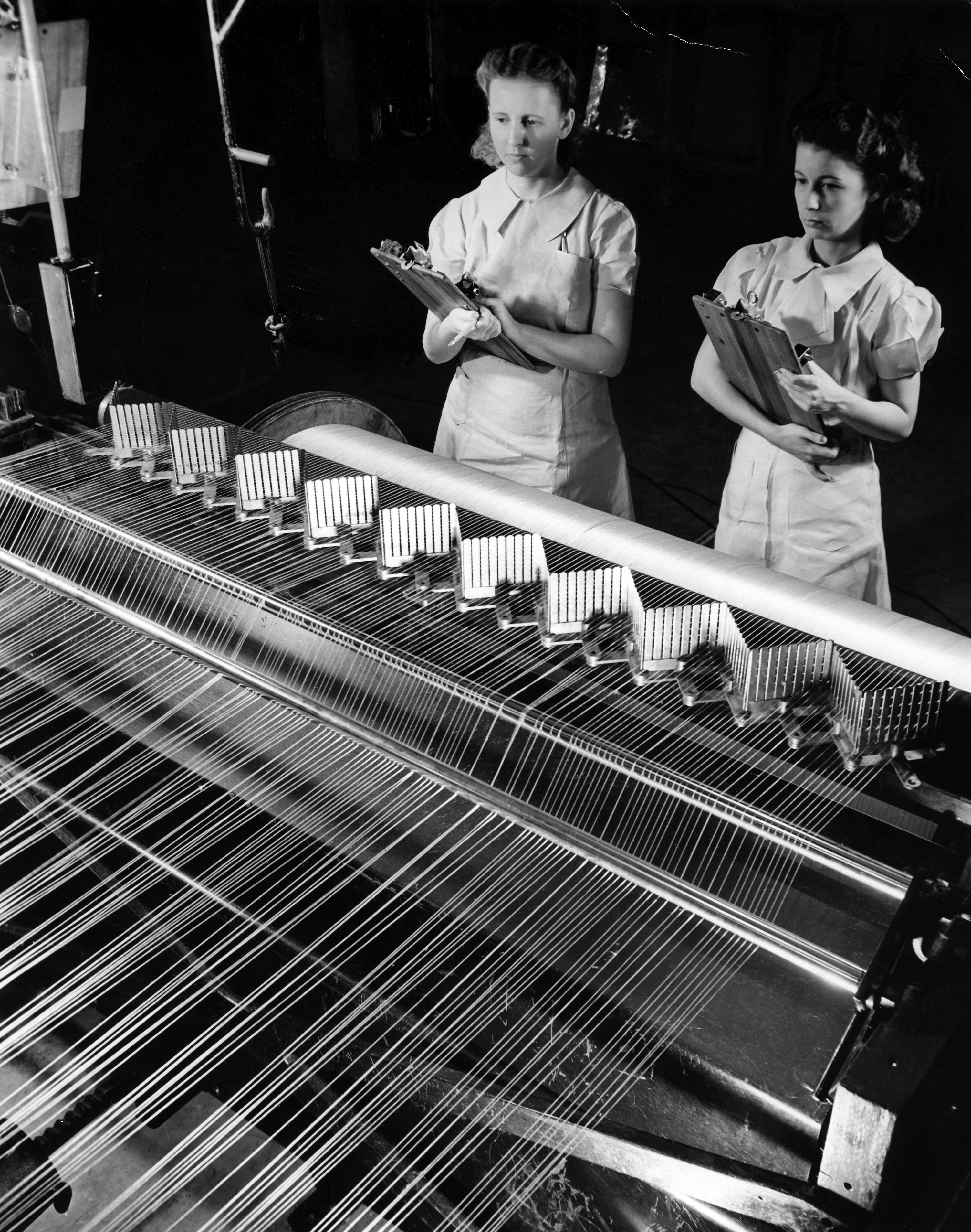 Black and white image of two women overseeing the manufacture of synthetic fibers on a machine.