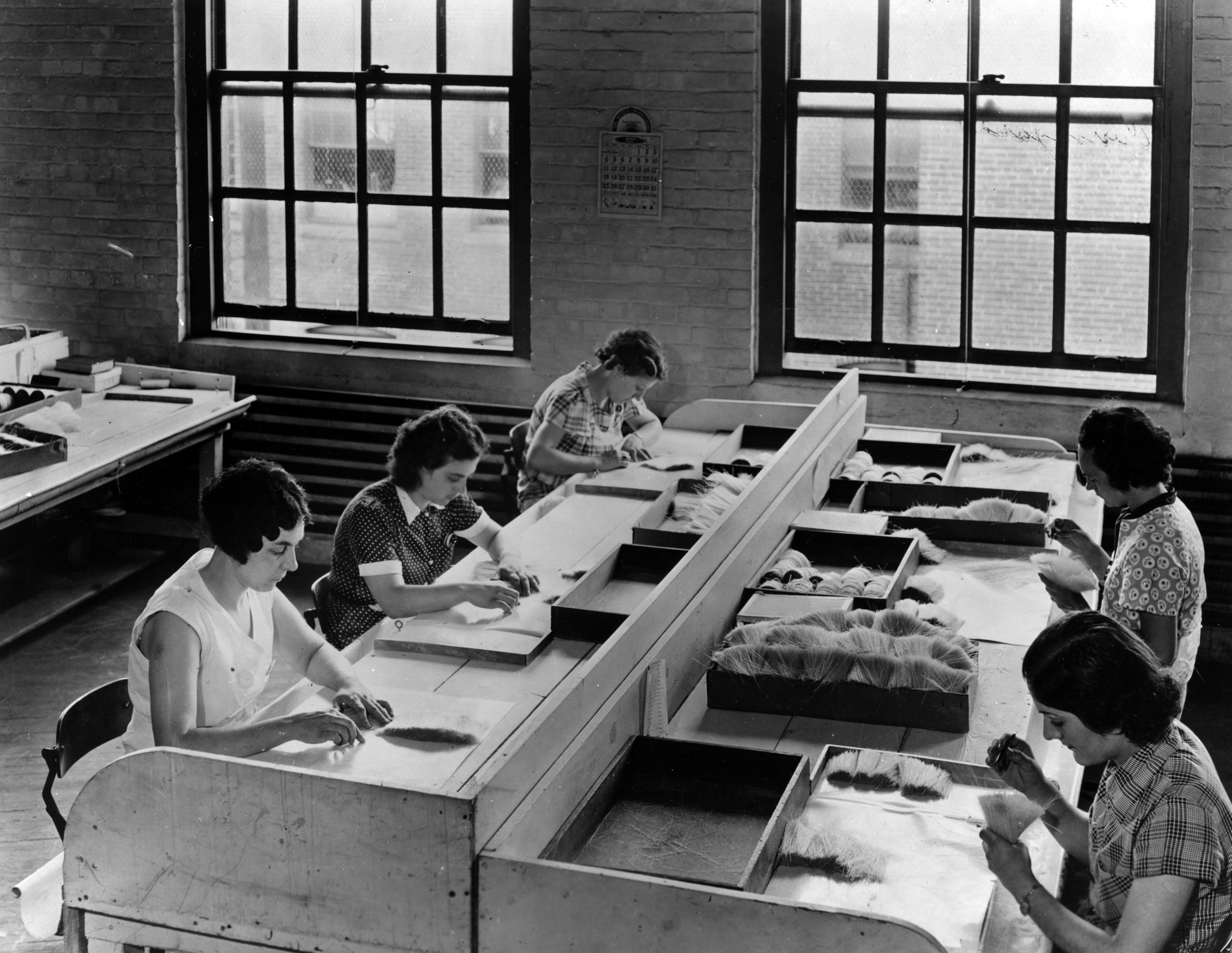 Black and white photograph of women in a factory picking out black and yellow bristles from the washed white stock.