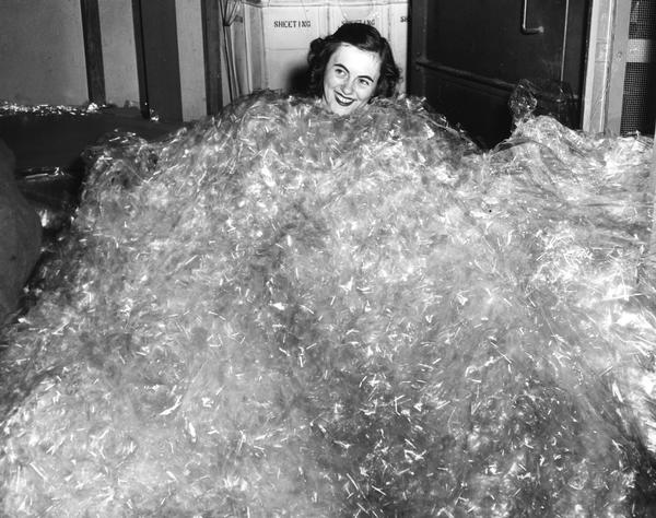 Black and white image of a woman buried up to her neck in crumpled cellophane.