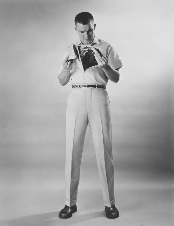 Black and white fashion photograph of a standing man reading 'Outdoor Life' magazine.