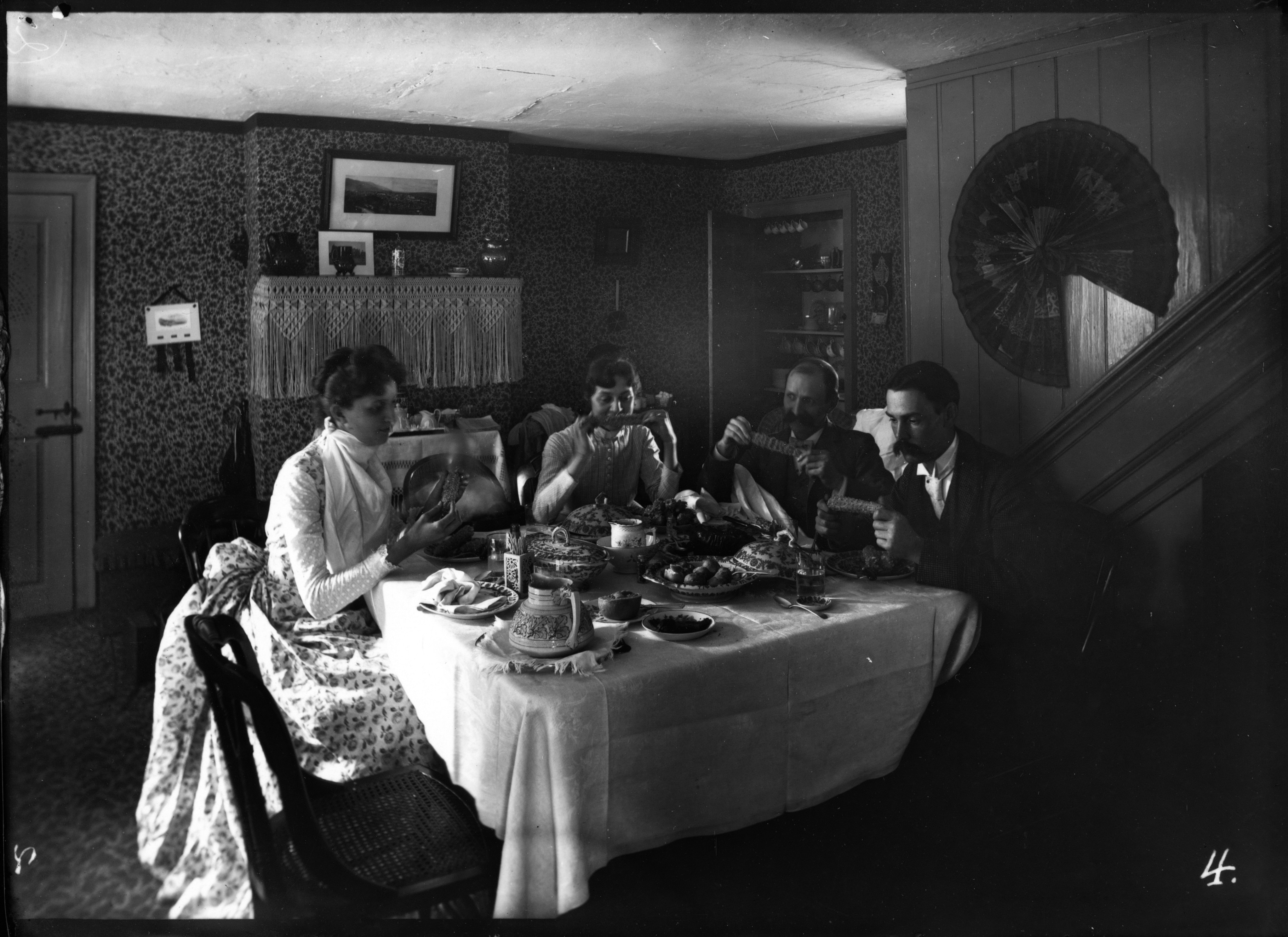 Black and white negative of two men and two women sharing a meal at a well-set table.