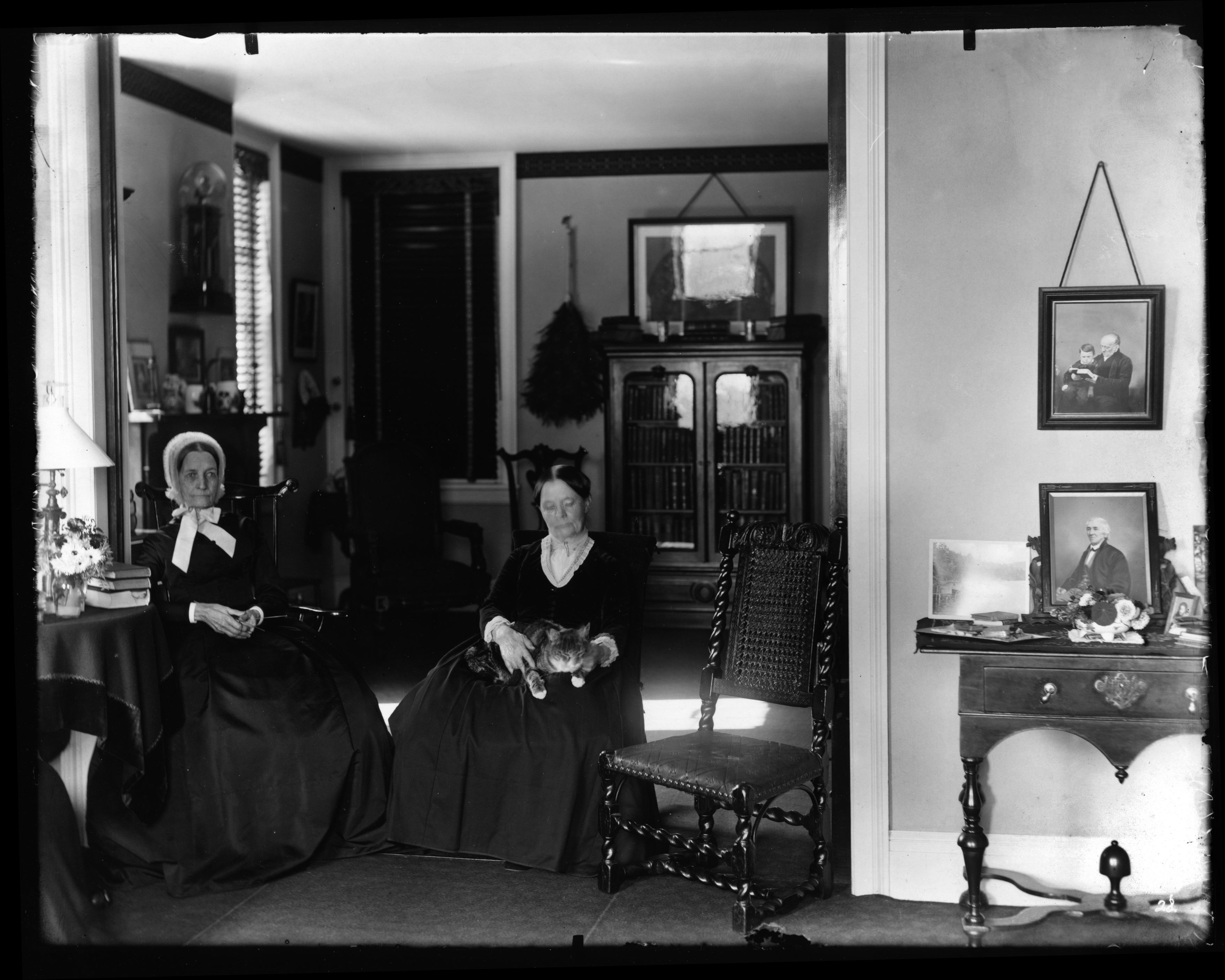 Black and white image of two seated women in a domestic setting. One has a cat in her lap.