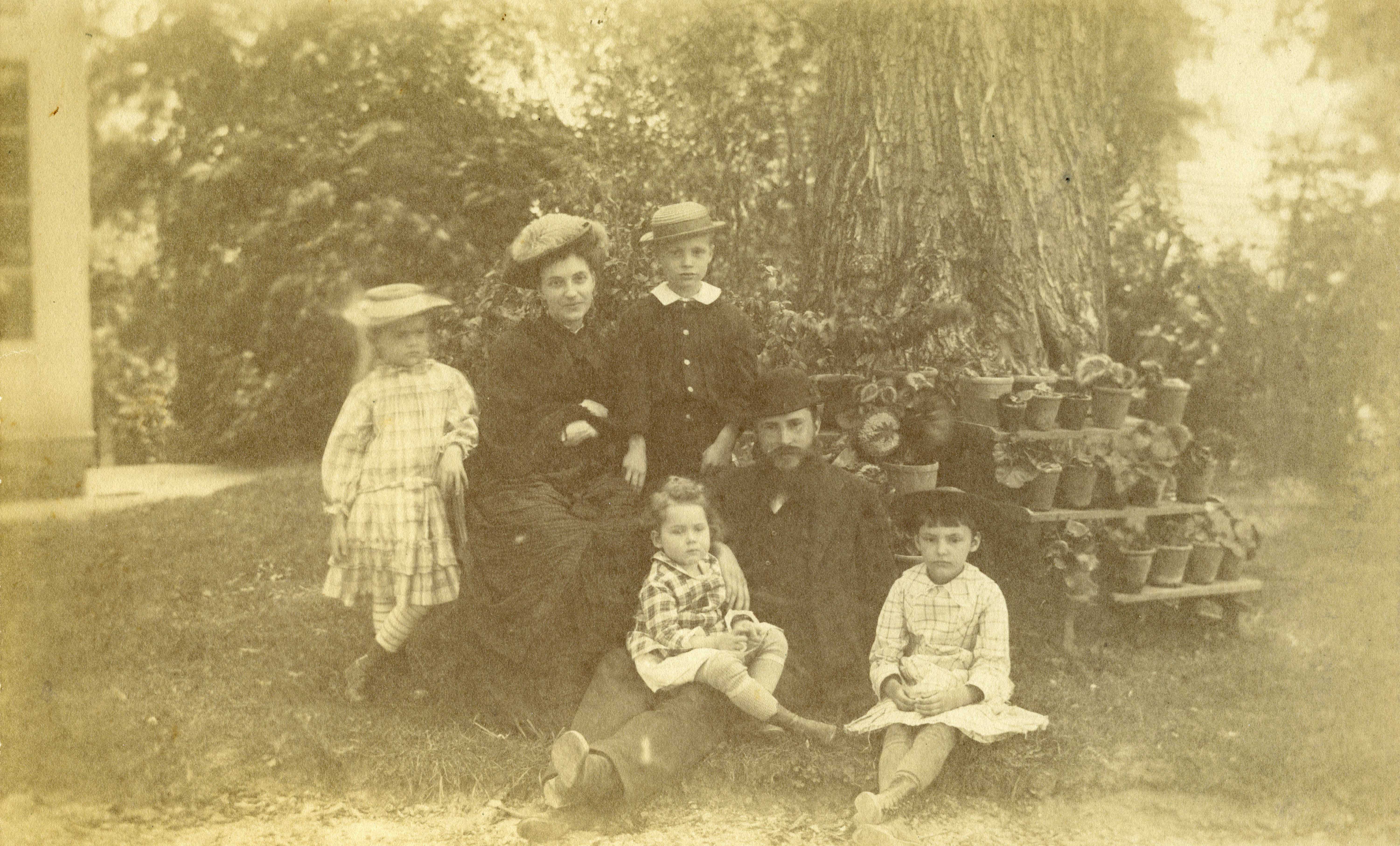 Sepia-tinged photograph of a family with small children, posed in a yard by a container garden