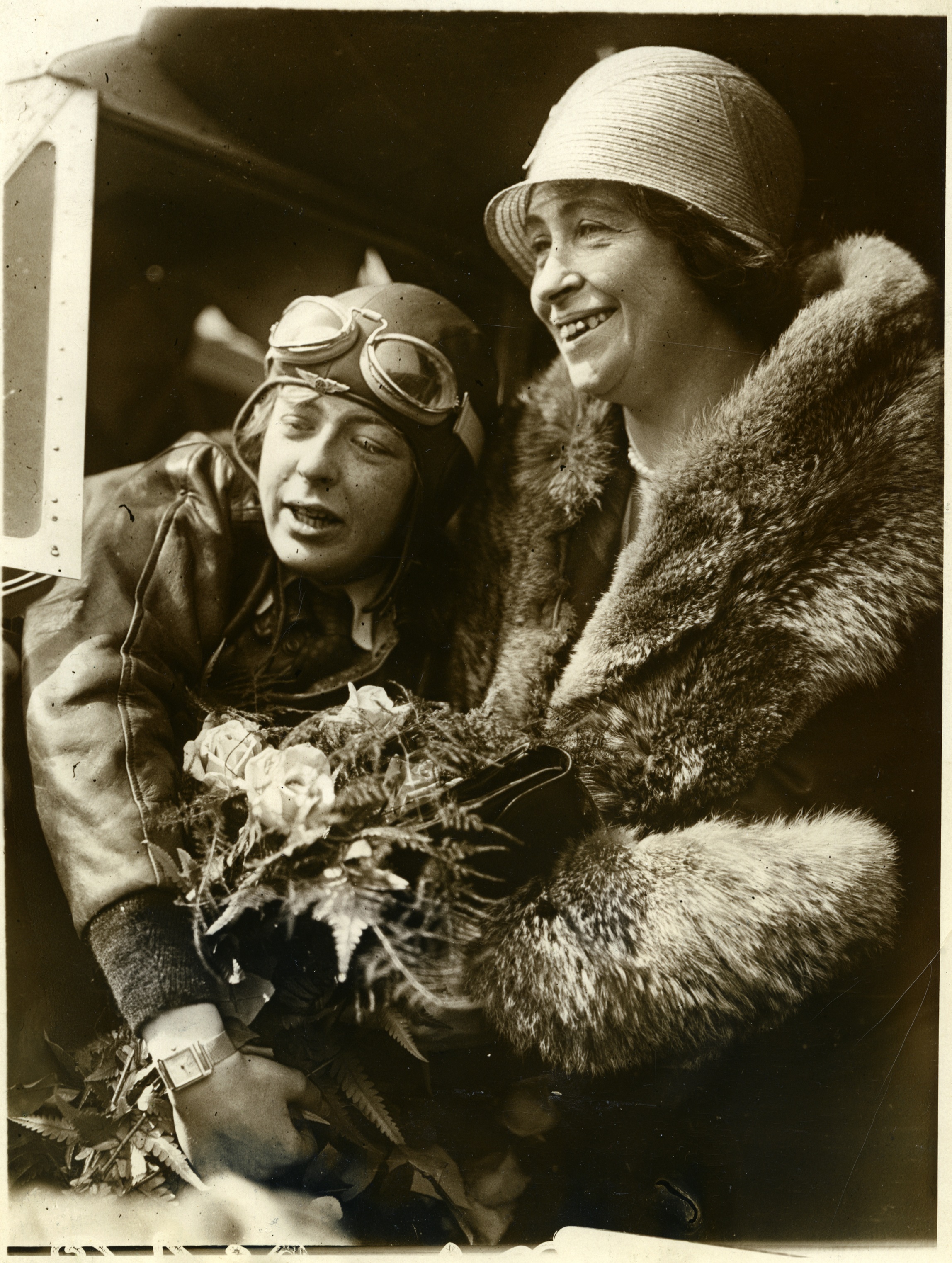 Black and white photograph of a woman in a pilot's gear hugging a woman holding flowers.