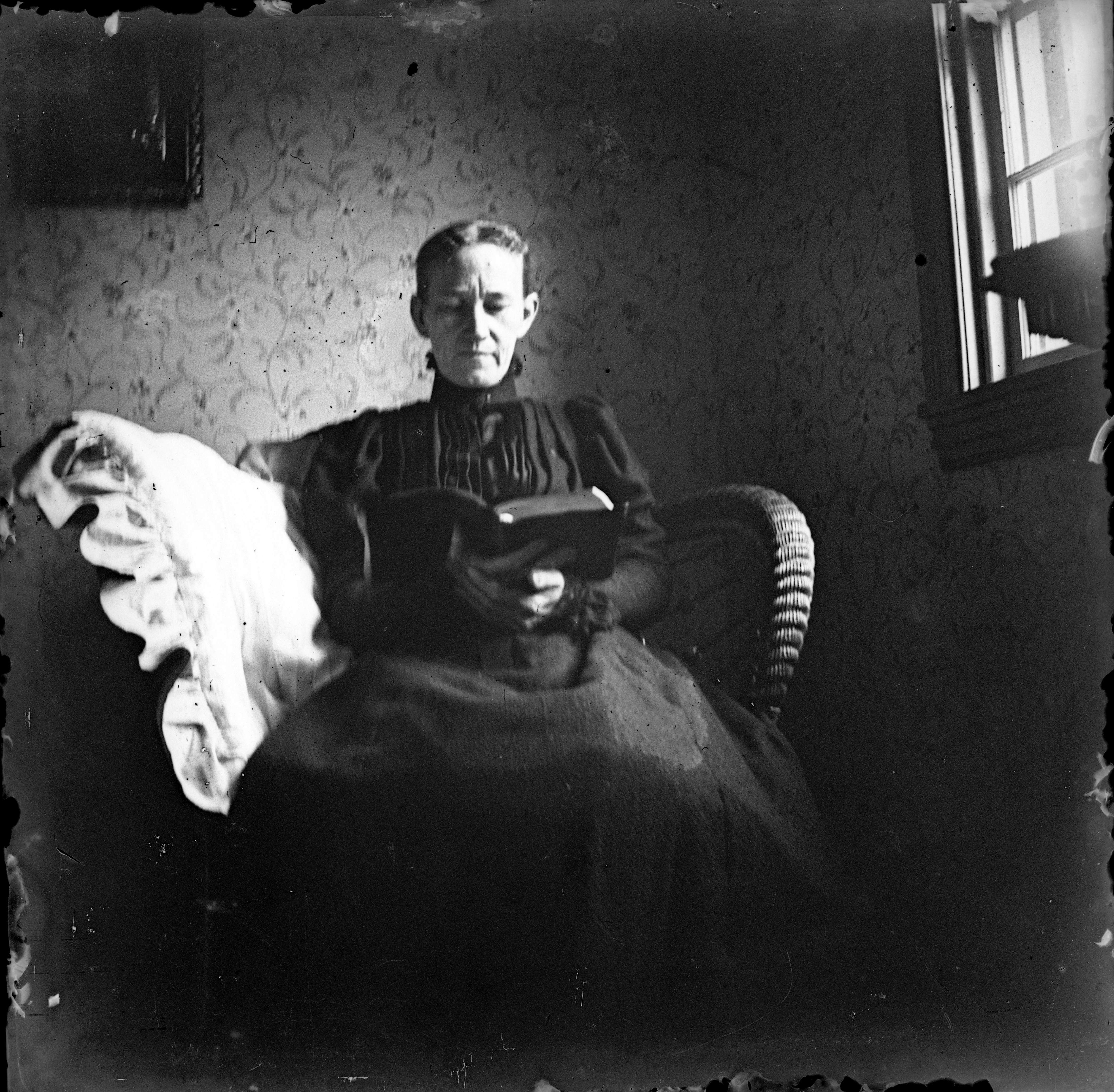 Black and white glass negative image of a seated woman reading a book.
