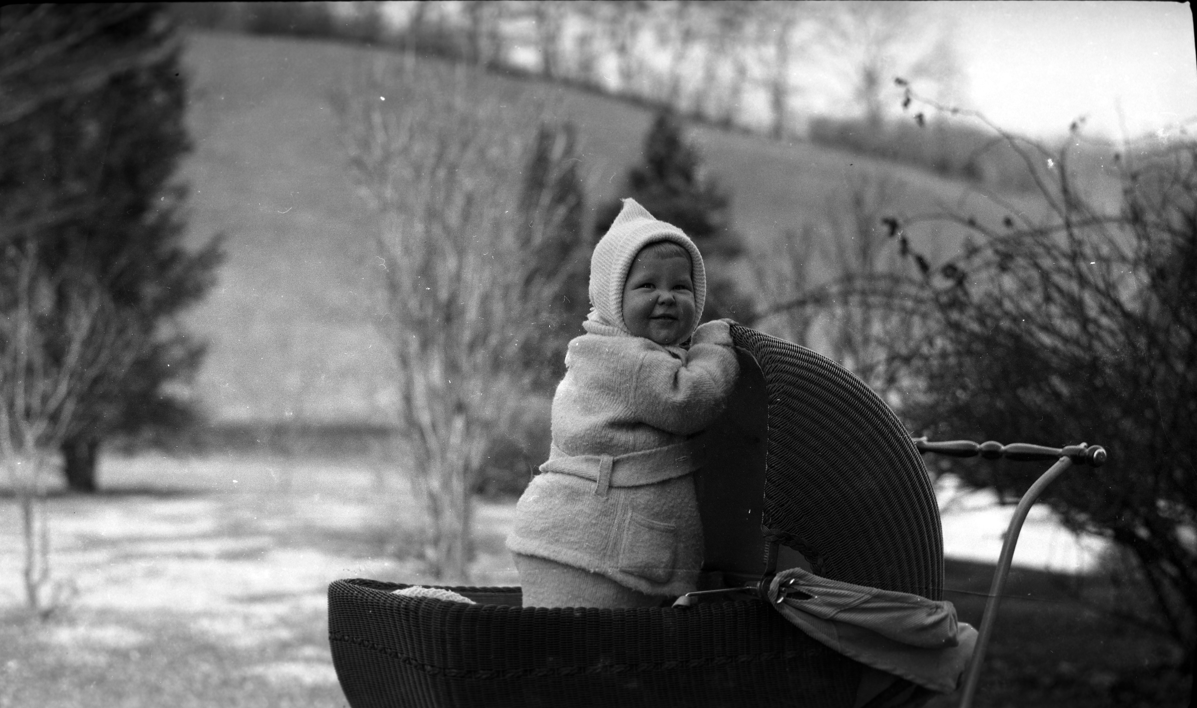 Black and white image of a baby bundled in warm clothing standing in his carriage