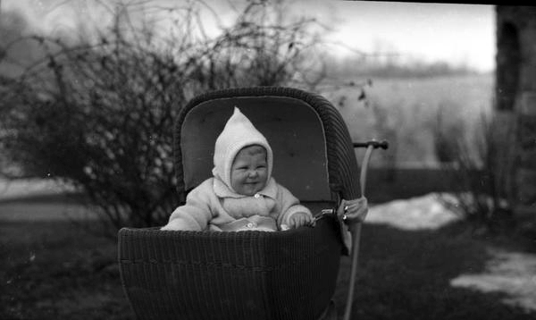 Black and white photograph of a baby, warmly dressed, in a baby carriage.