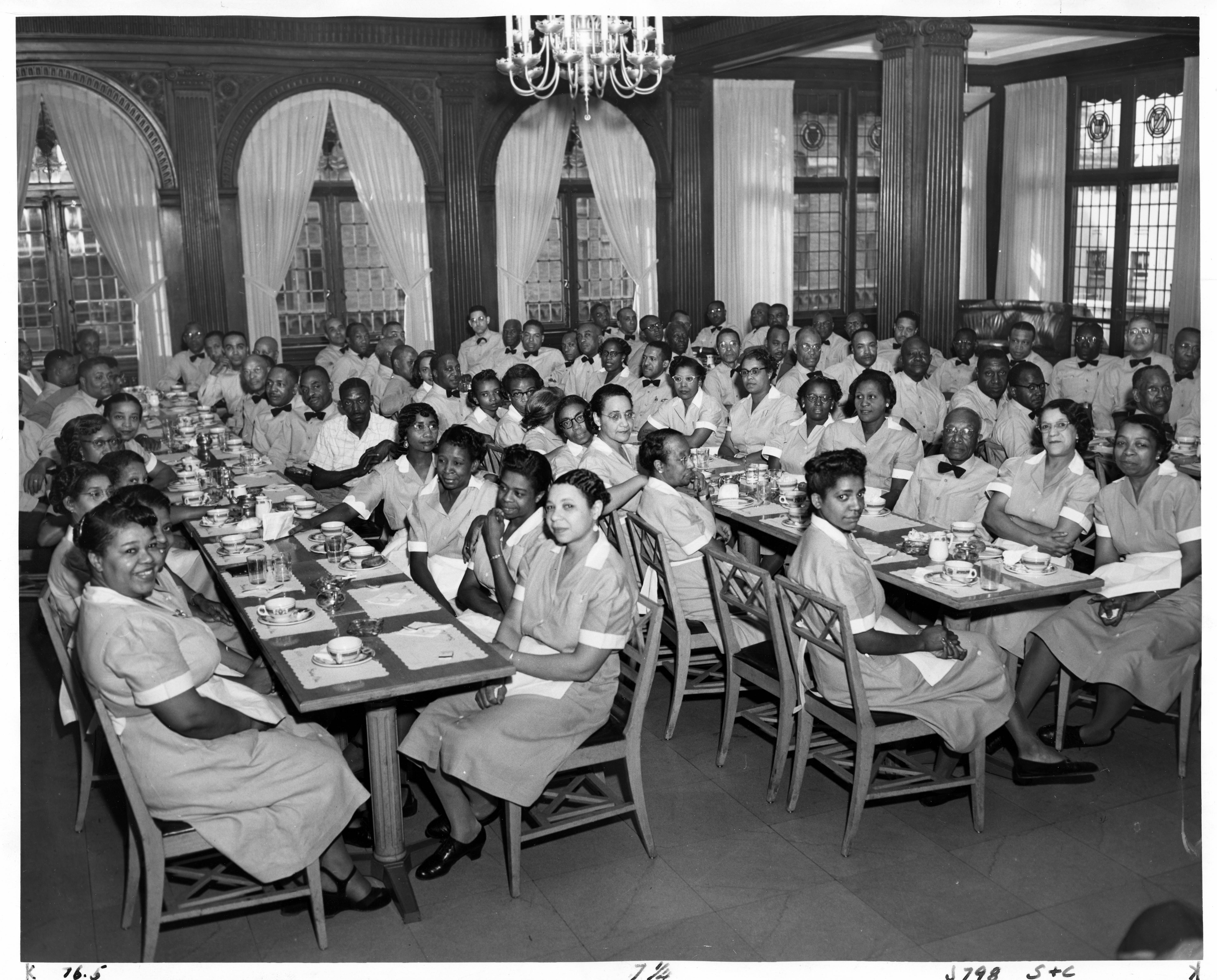 Black and white photograph of Black workers seated in the a dining room; all are wearing uniforms