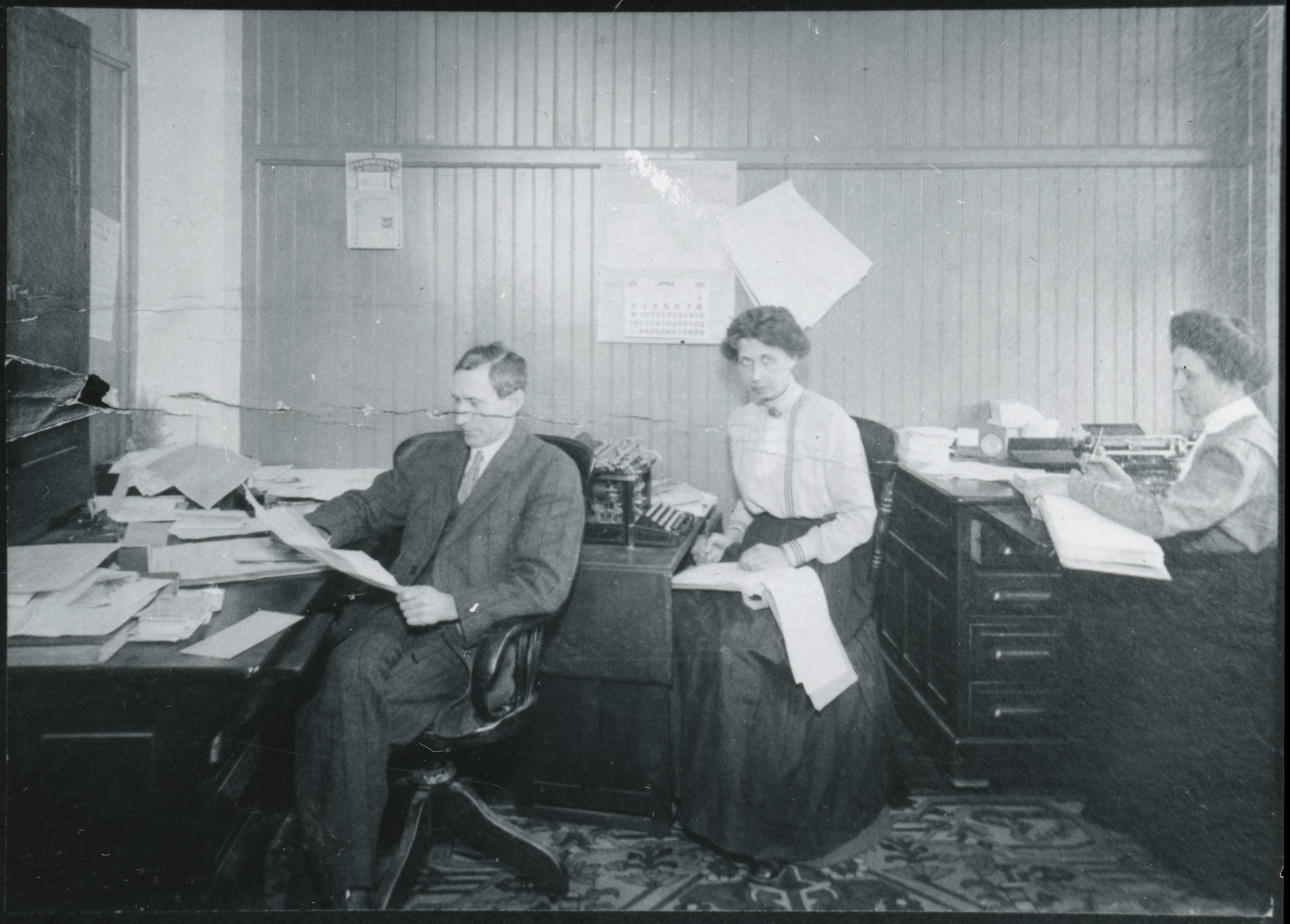 Black and white oimage of a man and two women working in an office, ca. 1910.