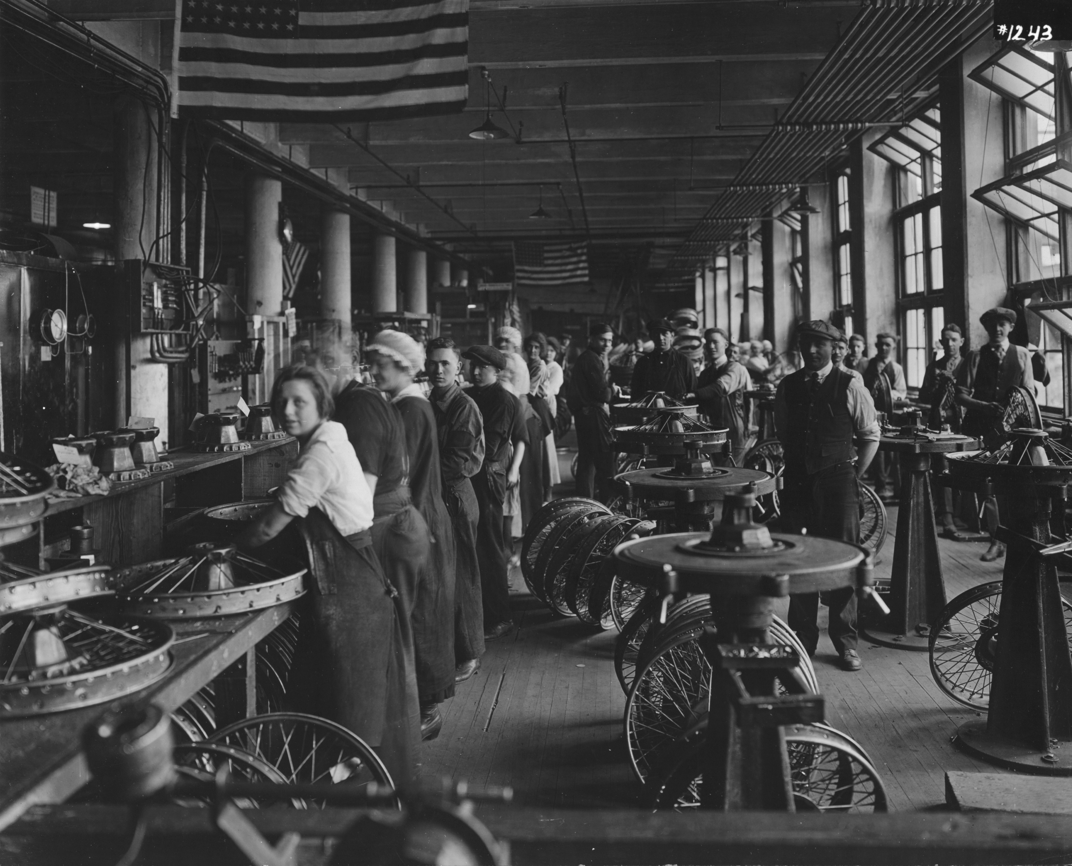 Black and white image of workers on assembly line in wheel factory