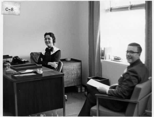 Black and white photograph taken inside an office inside the Hagley Library building. Left to right: Miss Betty Foster, Mr. Edward Ezell.