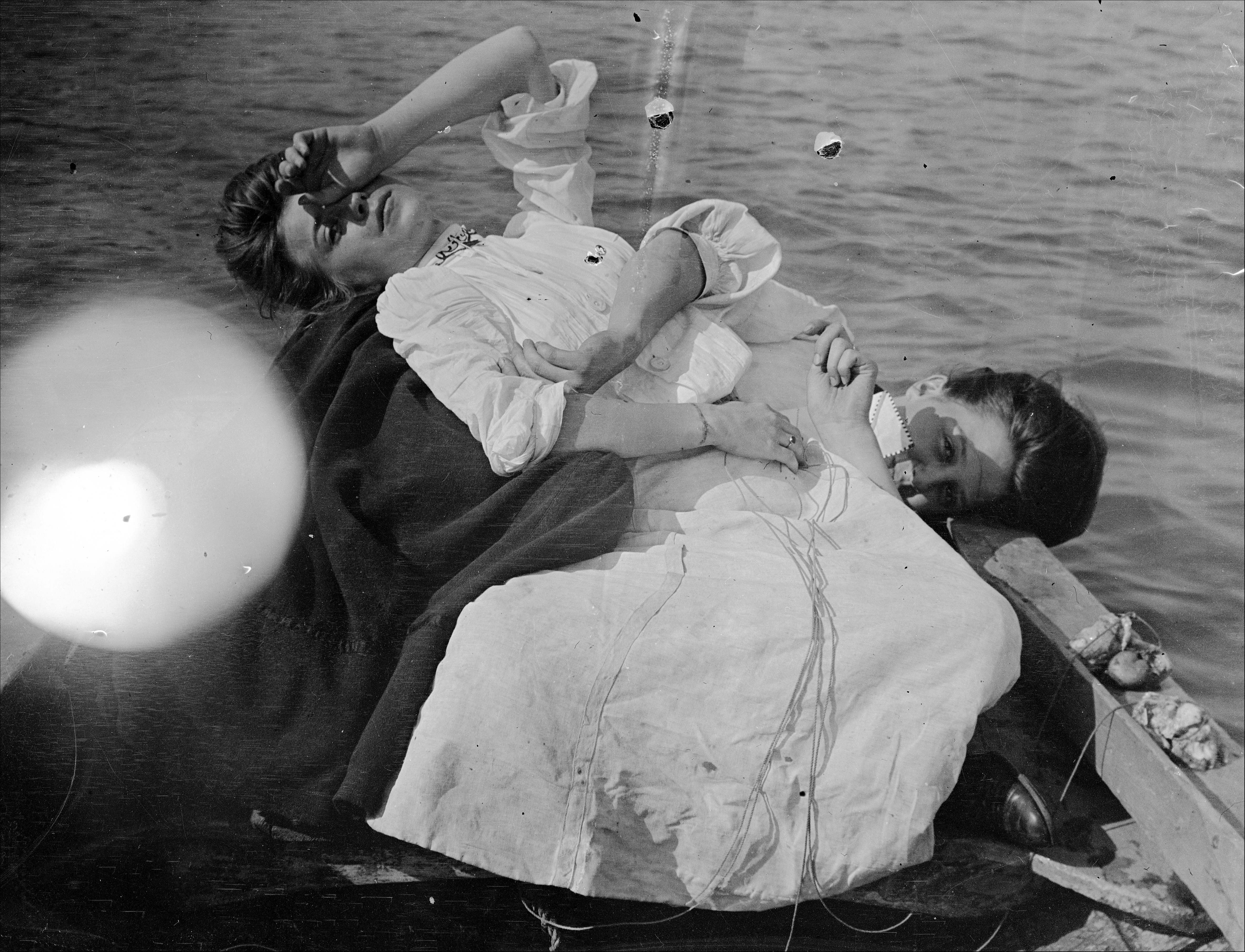 Glass negative image of two women in a rowboat, draped dramatically on top of one another.