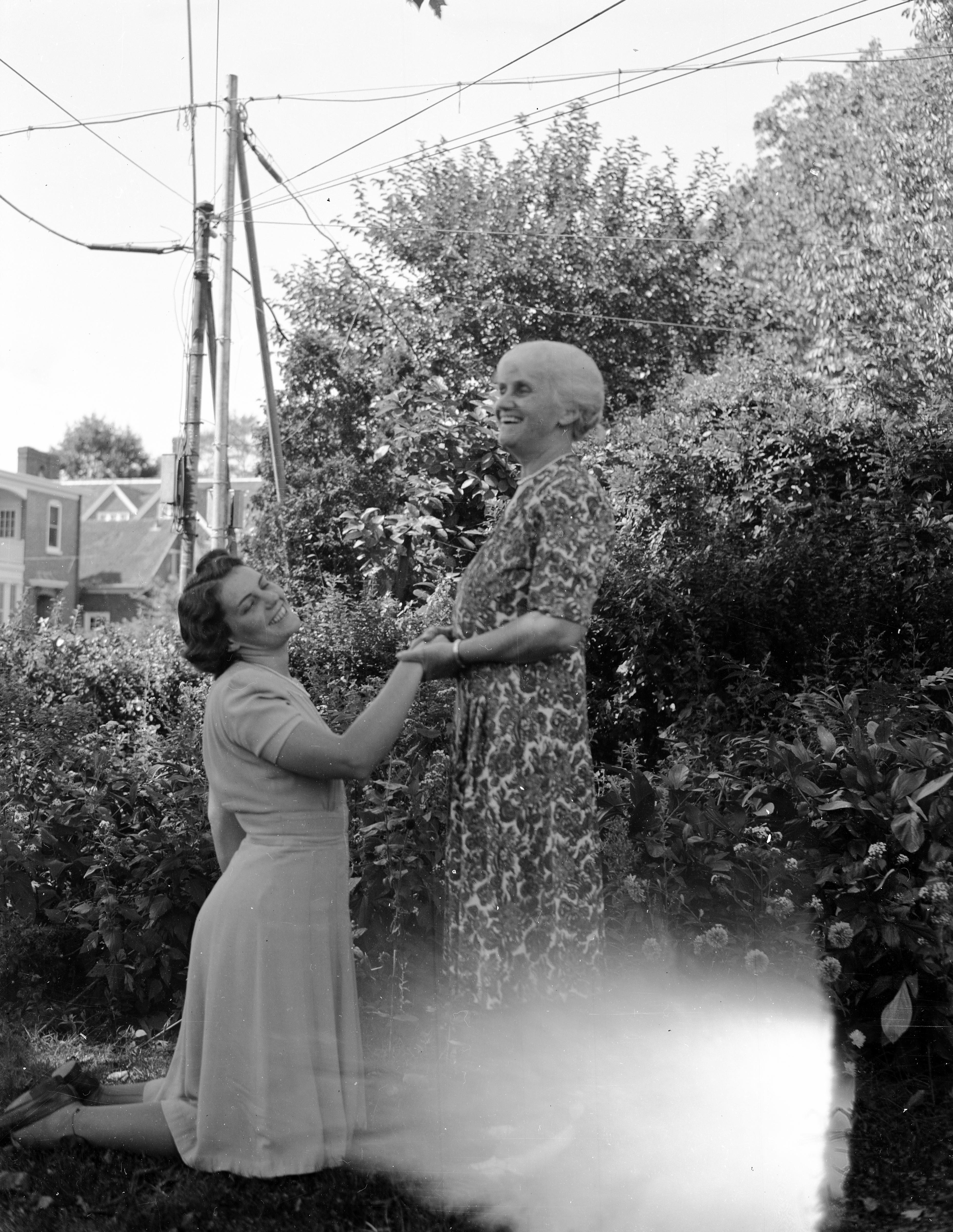 Two women holding hands and smiling. One is younger and kneeling, the other is older and standing.