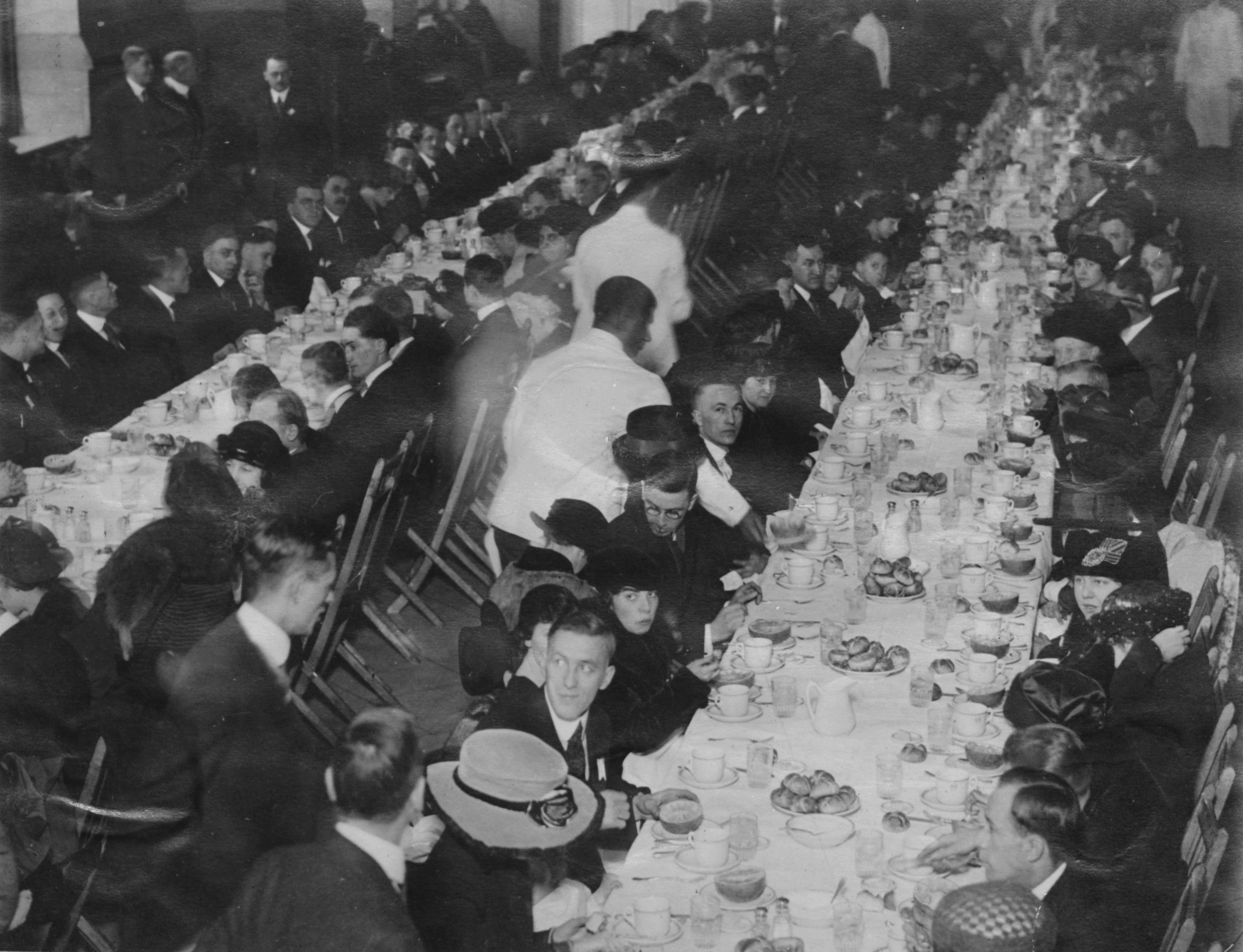 Two long rows of tables covered in breakfast foods with diners and wait staff.