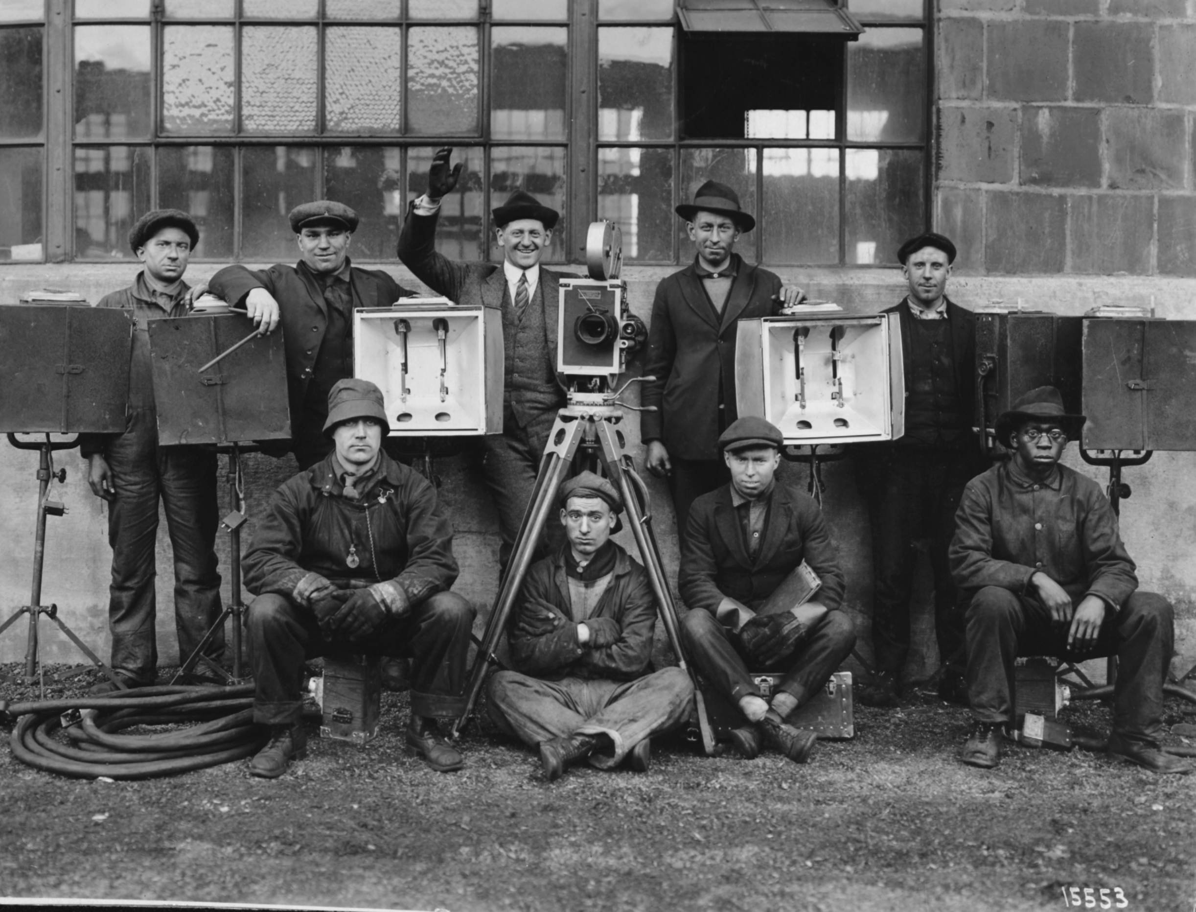 Black and white group photograph of nine men with motion picture equipment and cameras.