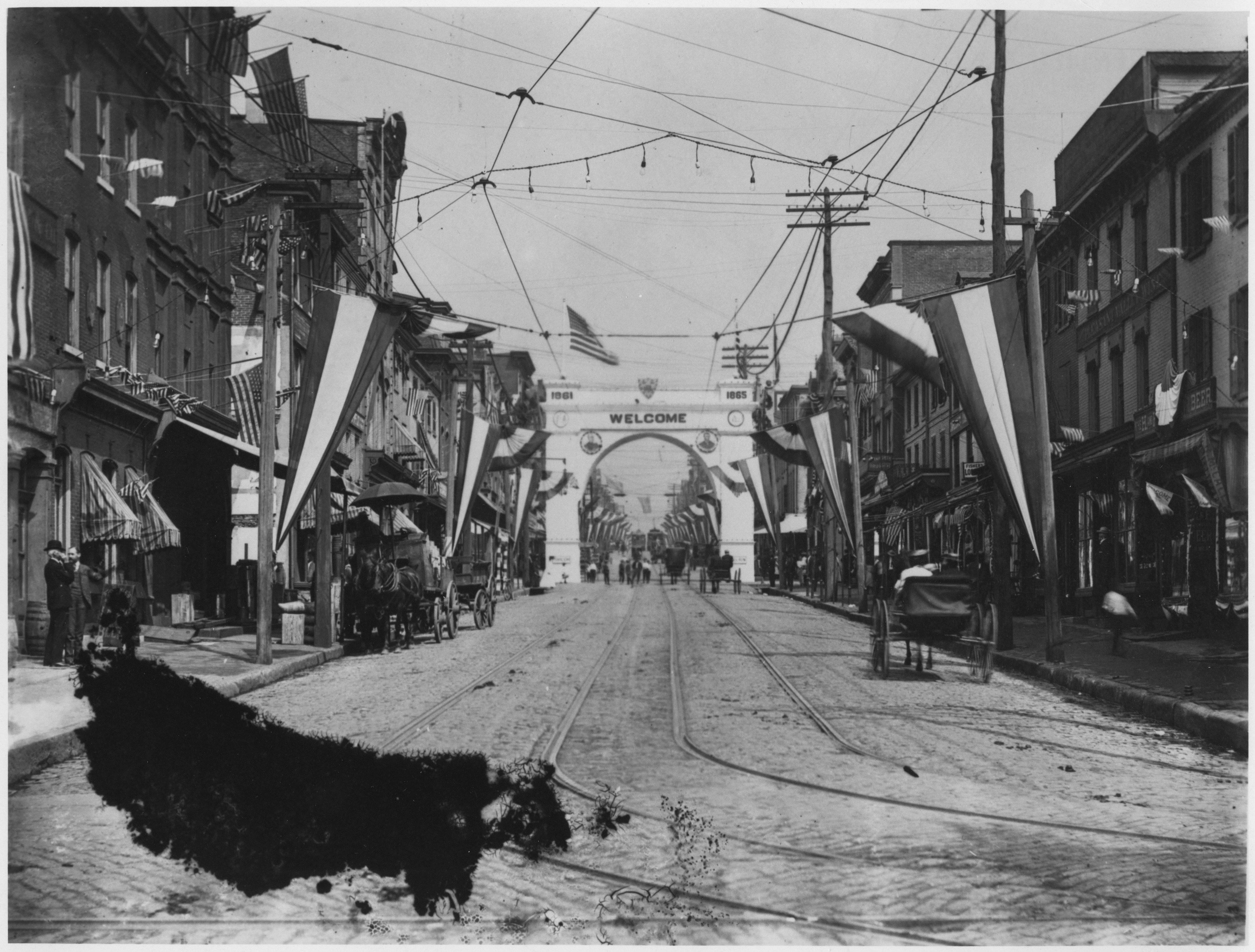 City street and an arch reading "Welcome" decorated in patriotic bunting and American flags