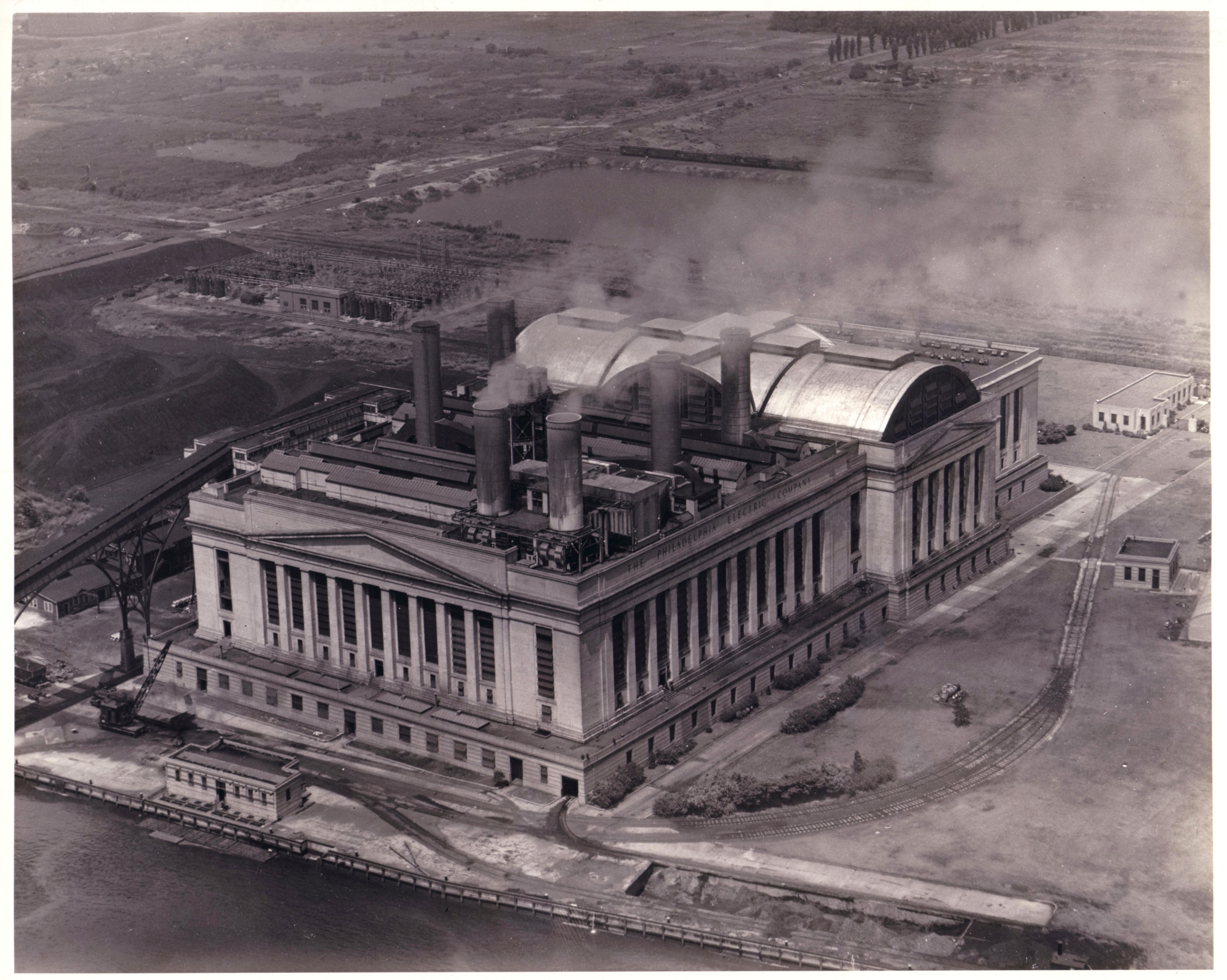 Black and white aerial photograph of a large electric plant located along a river.