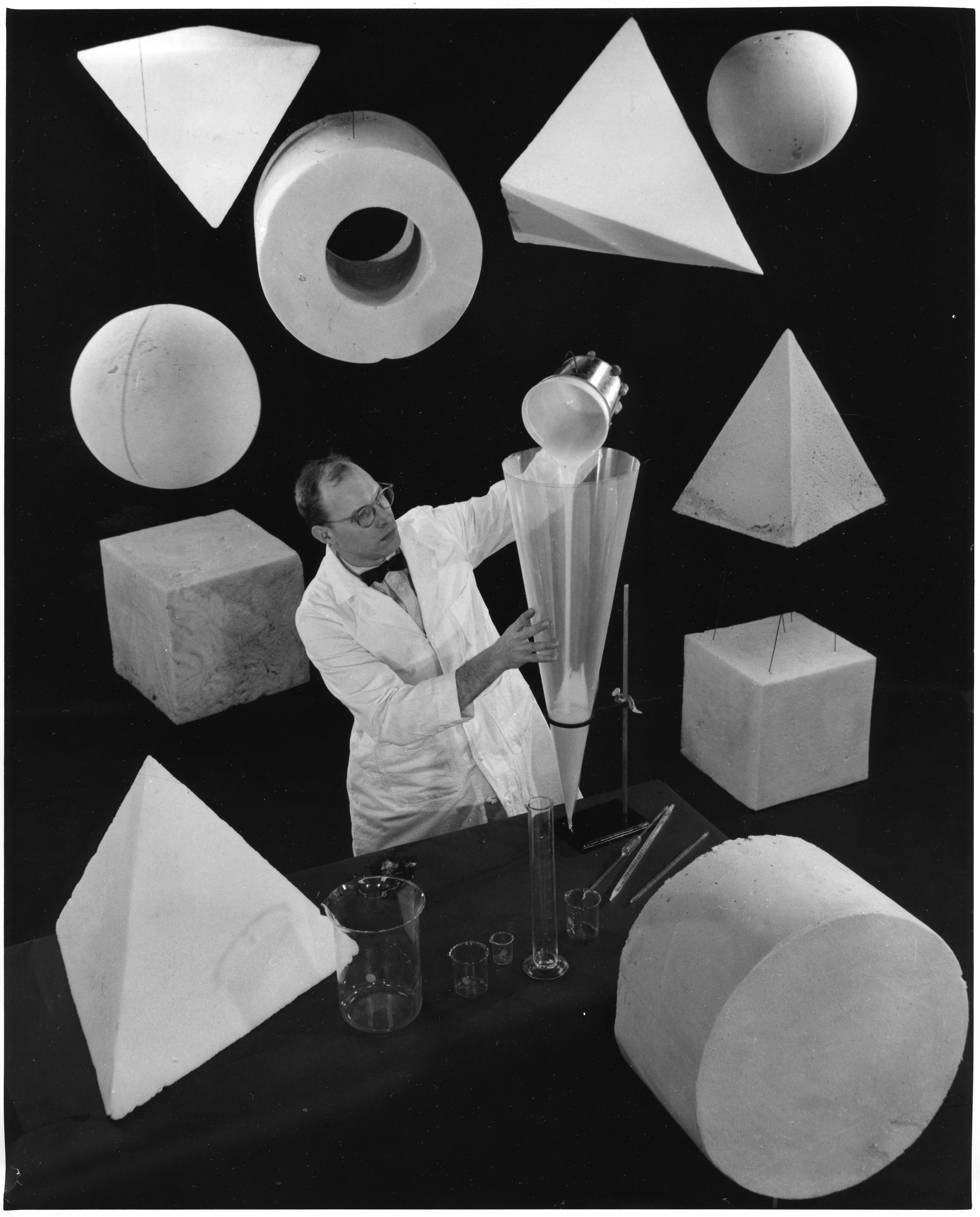 Black and white image of a scientist and scientific apparatus, surrounded by large foam and rubber shapes.