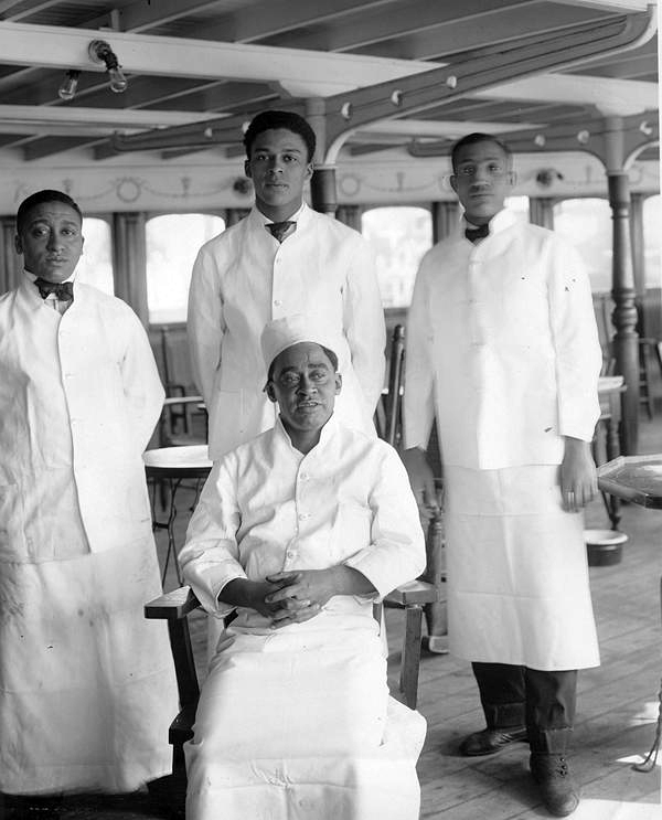 Group photograph of four people in professional kitchenwear on board a boat.