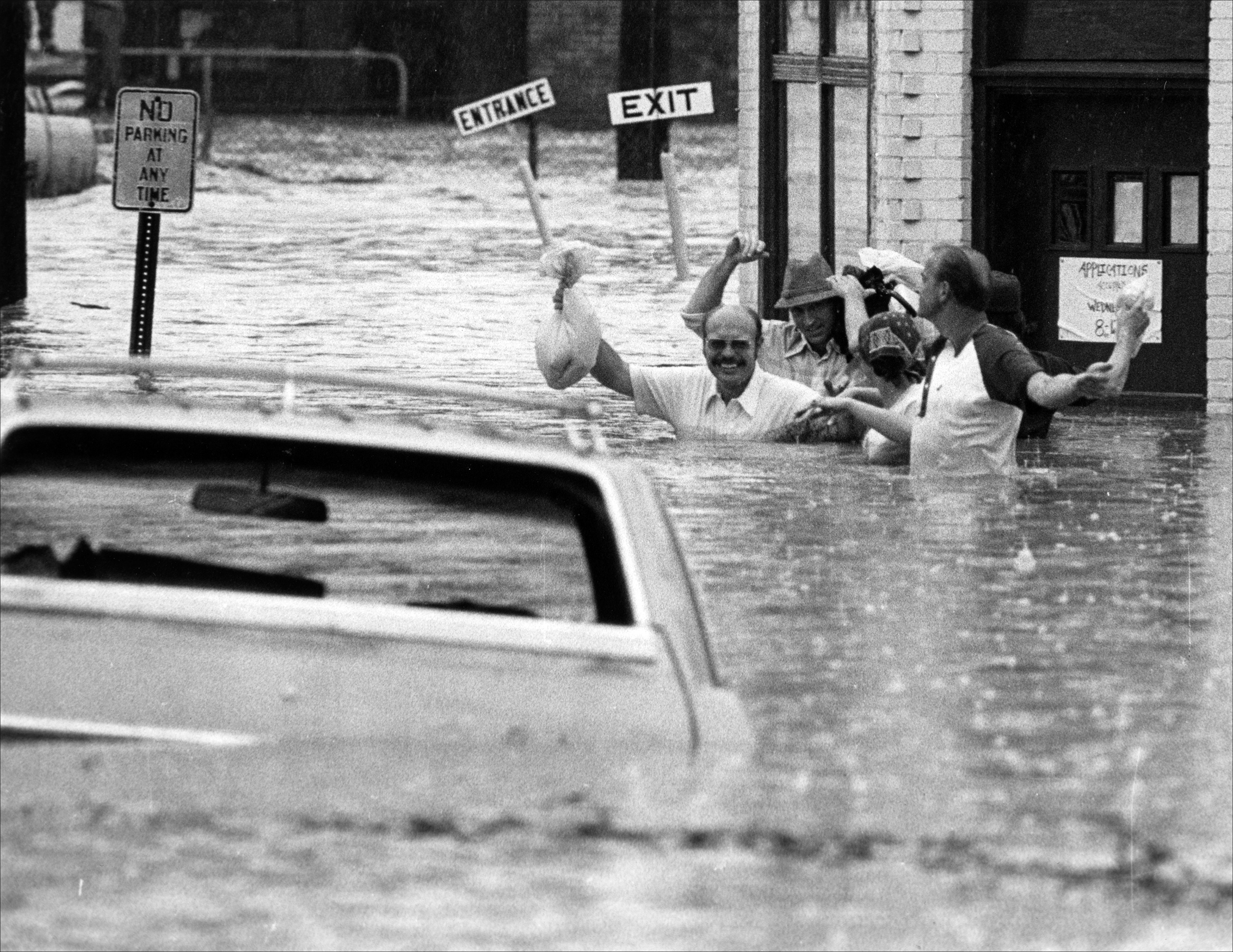 Black and white photograph of a group of men wading through heavily flooded streets.
