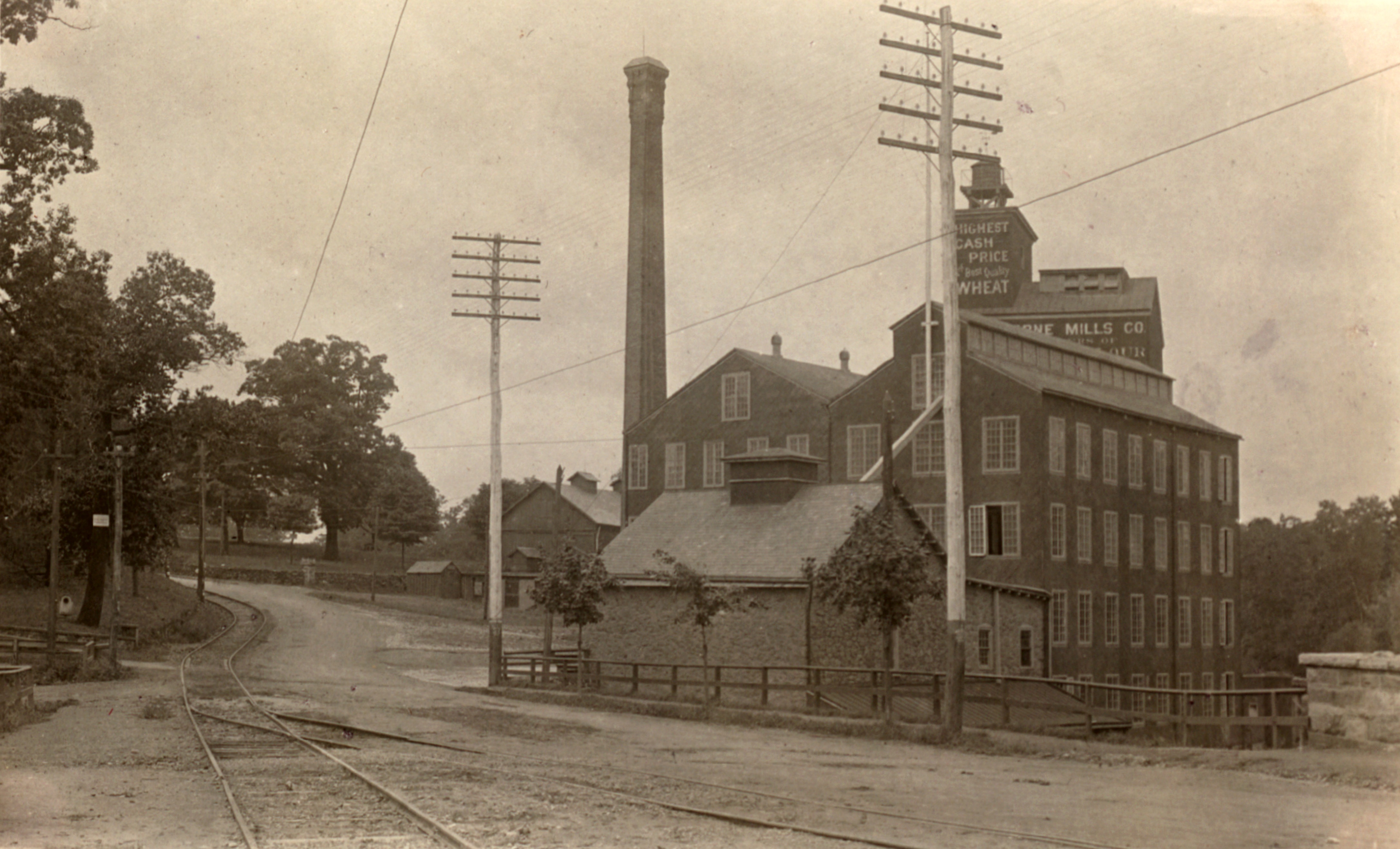 Black and white photograph of a railway track and road alongside a grain-milling factory.