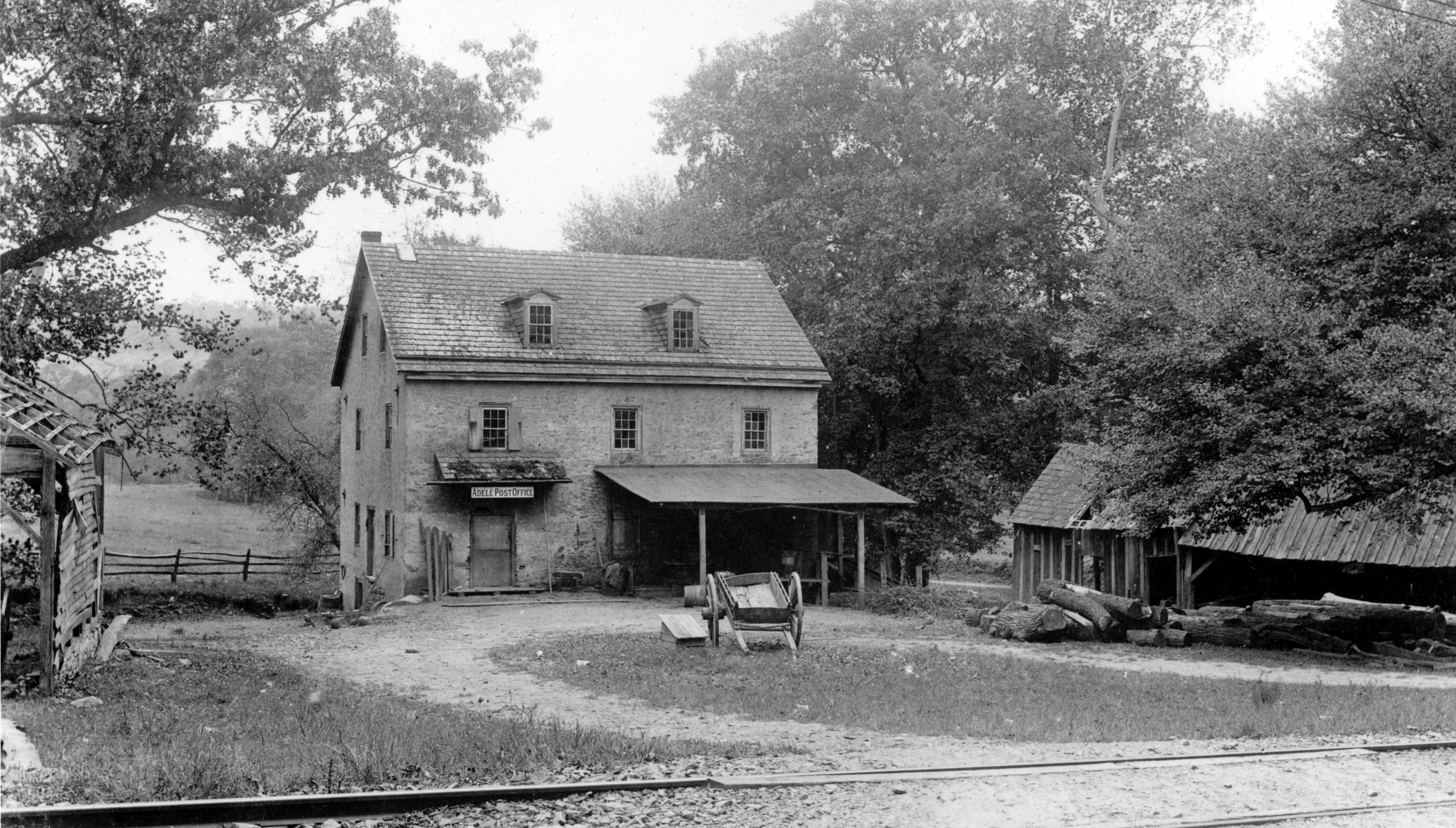 Black and white image of a ca. 1900 rural post office building fronted by railroad tracks.