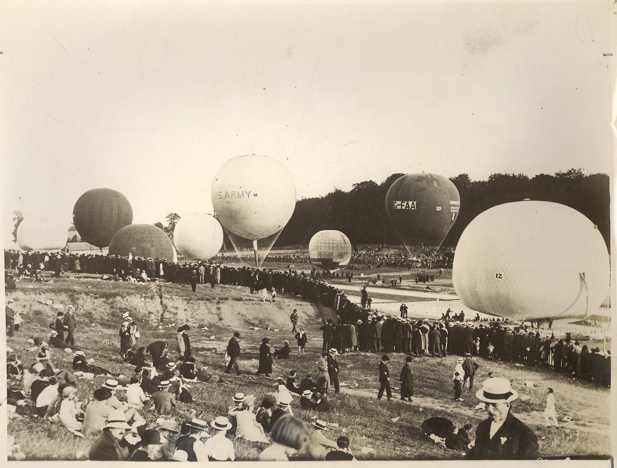 Black and white image showing a crowd assembled at the start of a hot air balloon race. A number of grounded balloons are in the image.