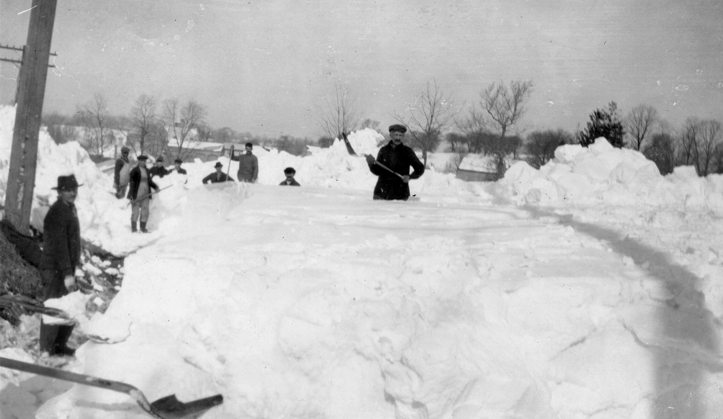 Black and white image of a group of people shoveling a large amount of snow.