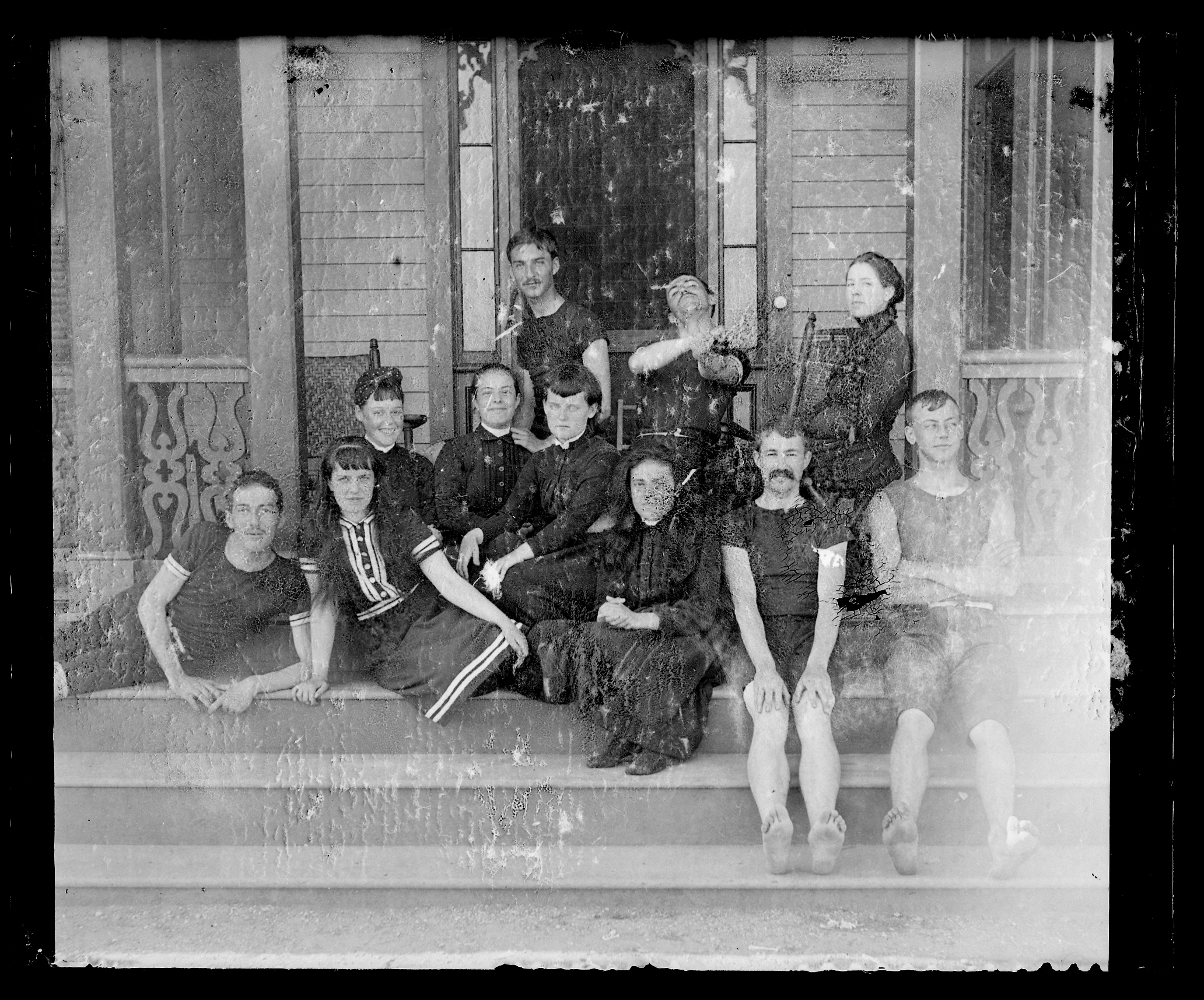 Black and white glass negative showing a group of young people in 1880s beachwear seated on porch steps.