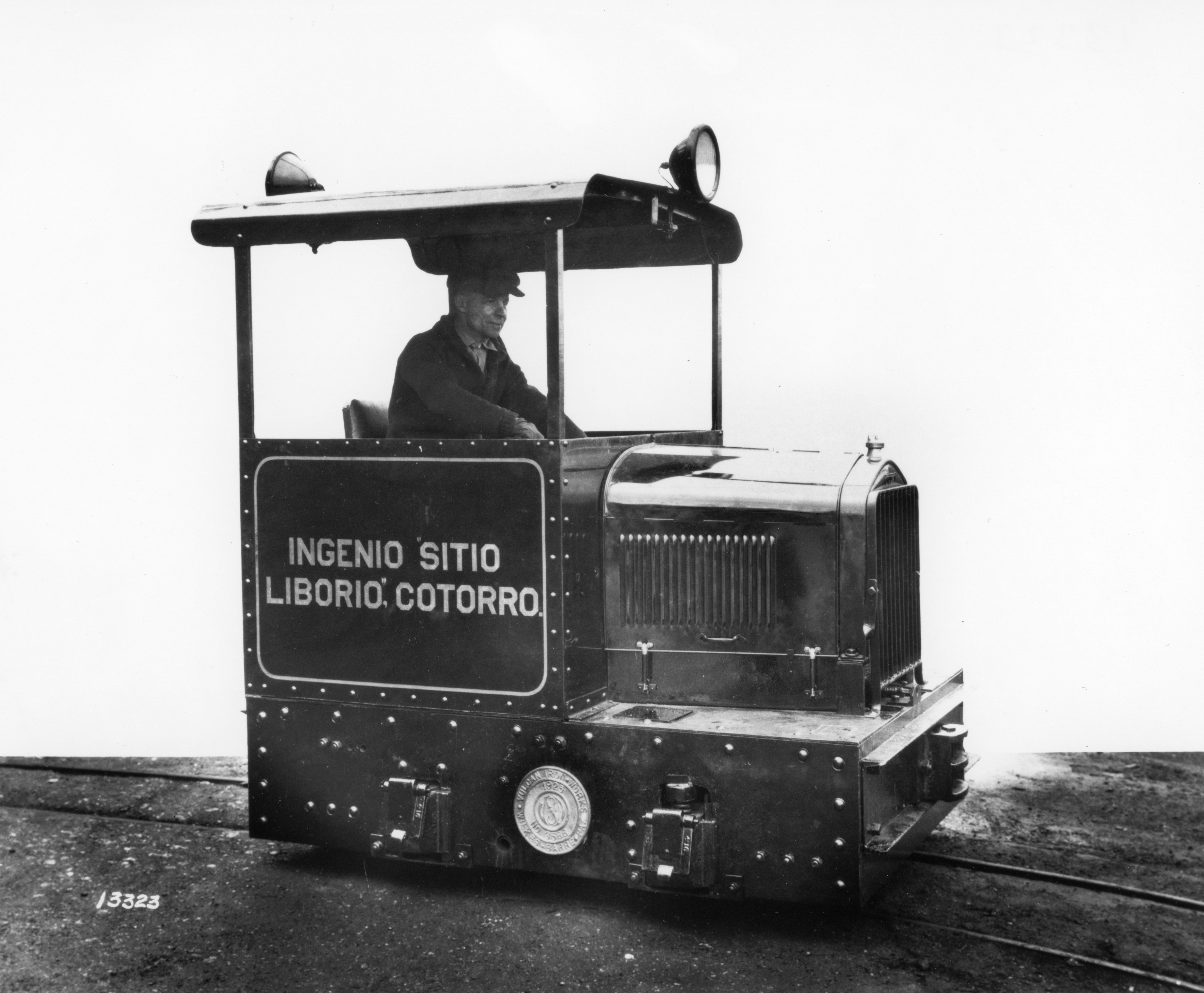 Black and white image of a man seated in a very small locomotive.