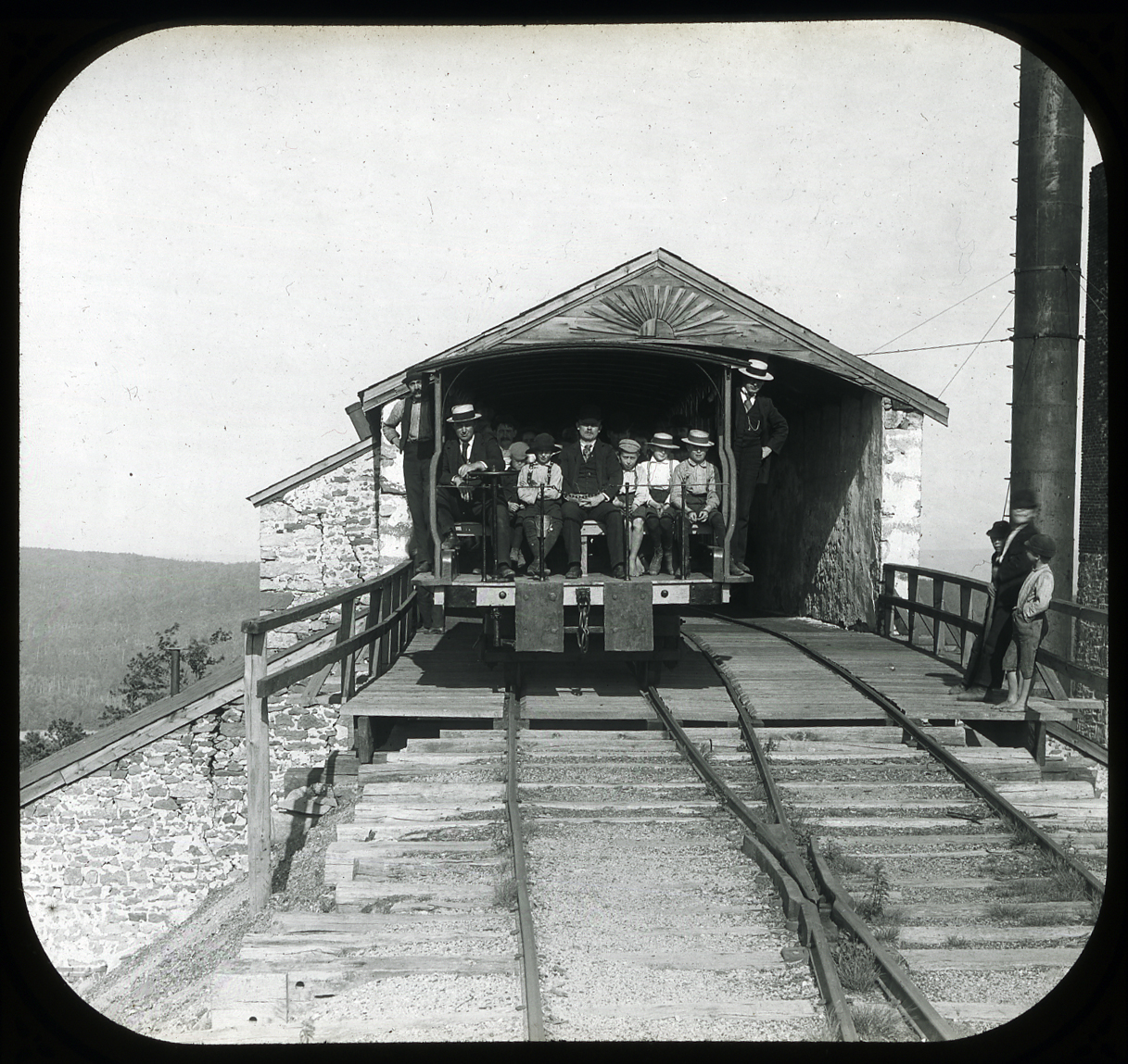 Black and white image of passengers in an open-backed train car.