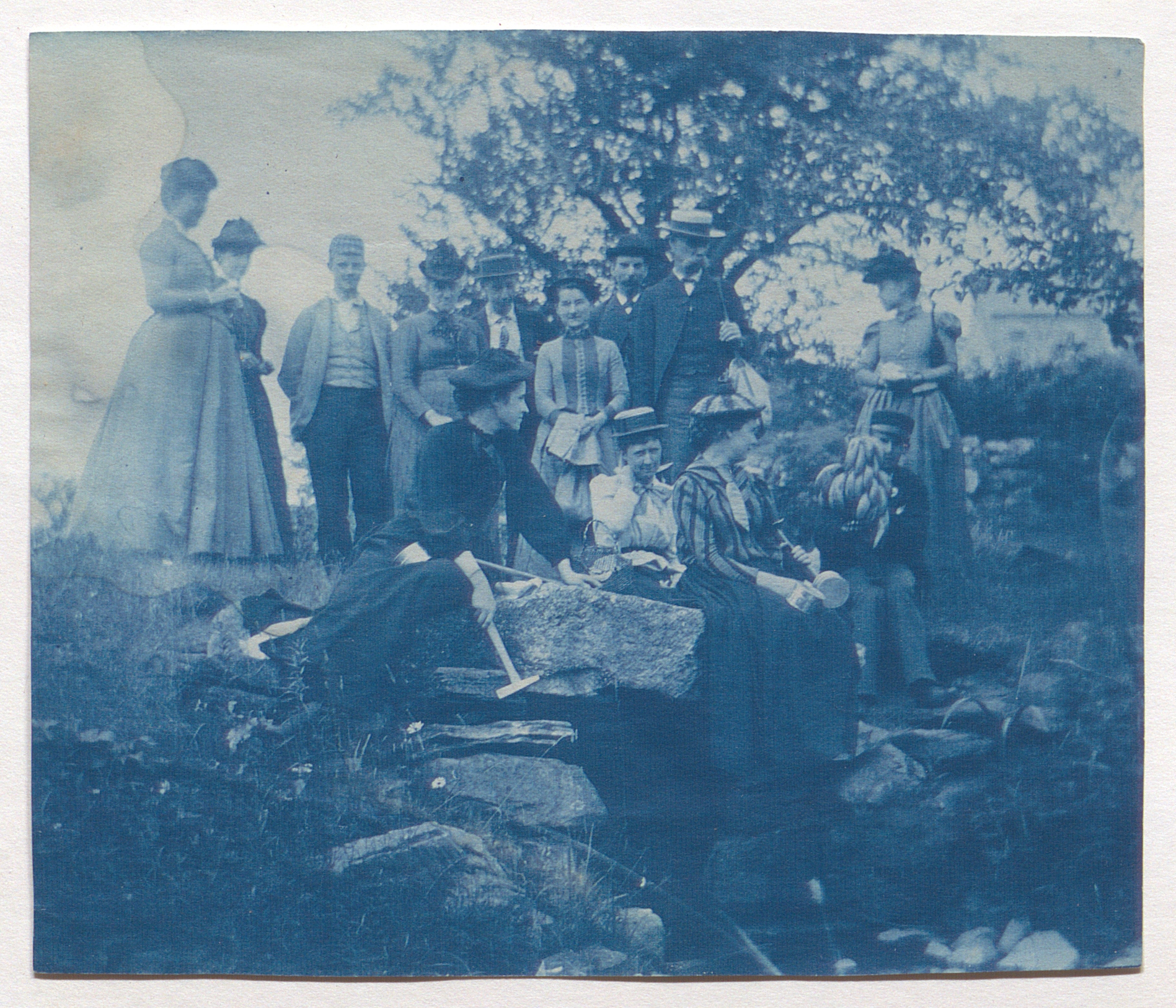 Cyanotype photograph of a group of people in an outdoors setting.