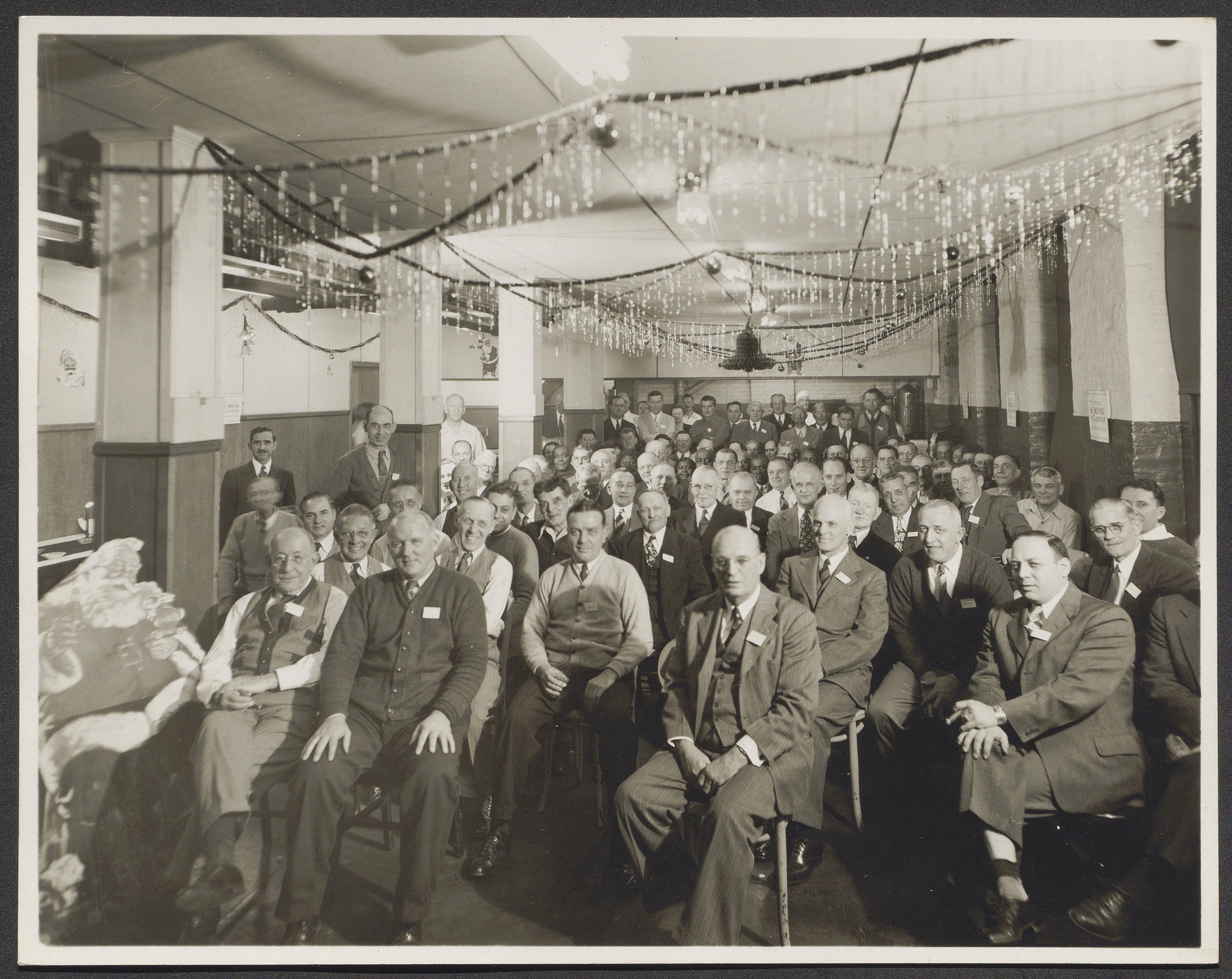 Black and white image of a large number of seated people in a room with Christmas decorations