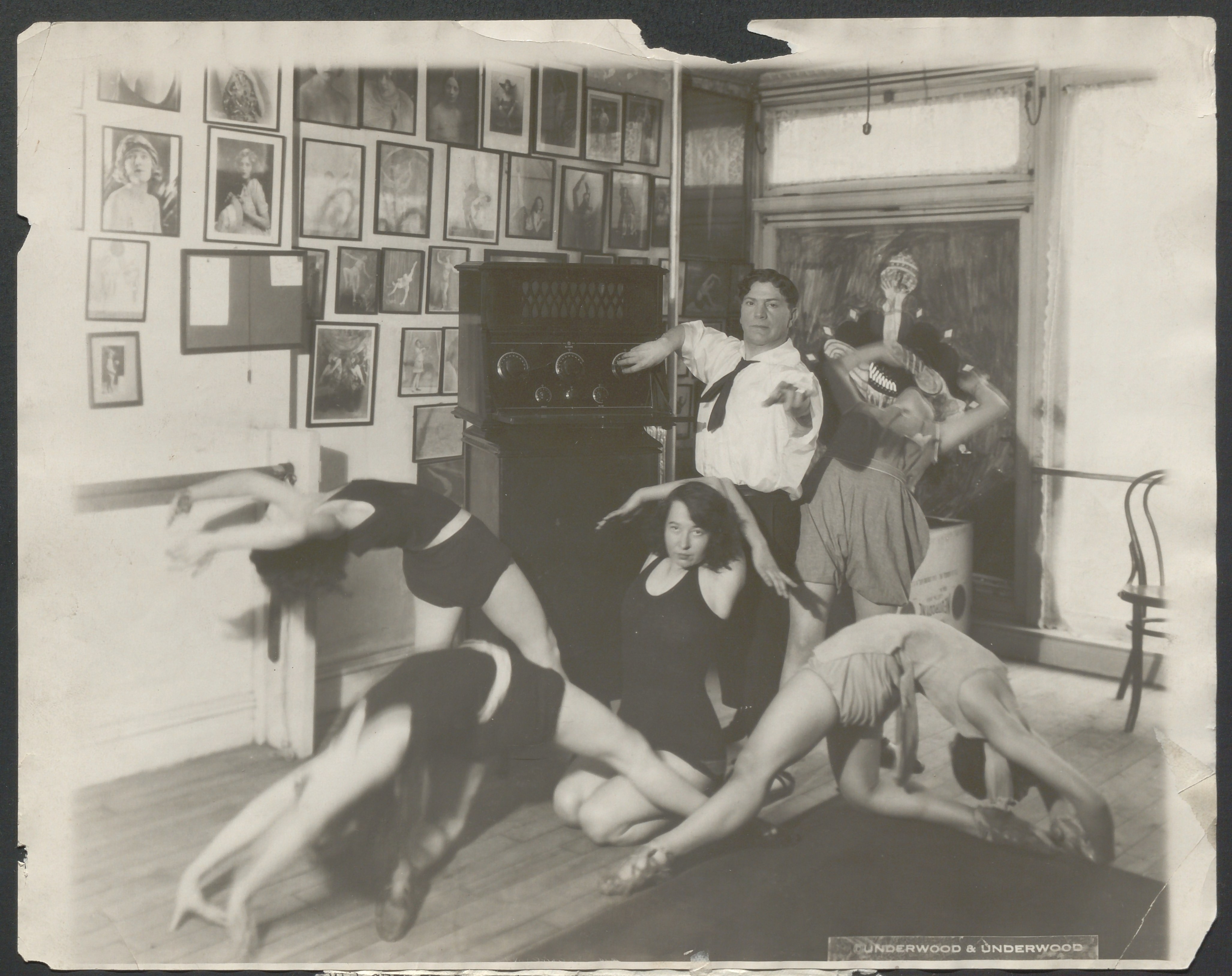 Black and white photograph of a man operating a radio console while surrounded by dancers in motion.