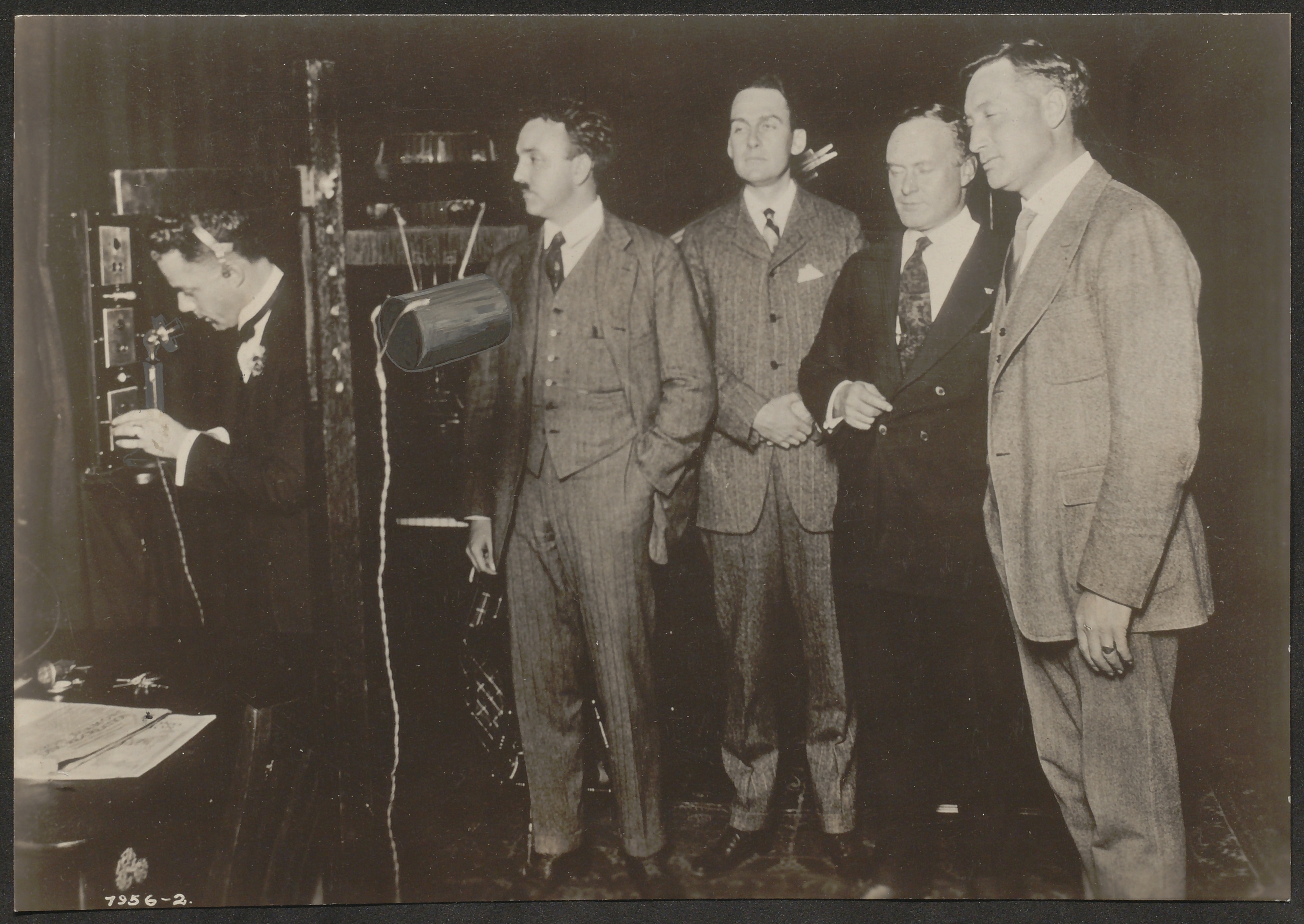 Black and white photograph of a musical pentet in a 1930s music studio. A can-shaped recording device has been emphasized with overdrawing.