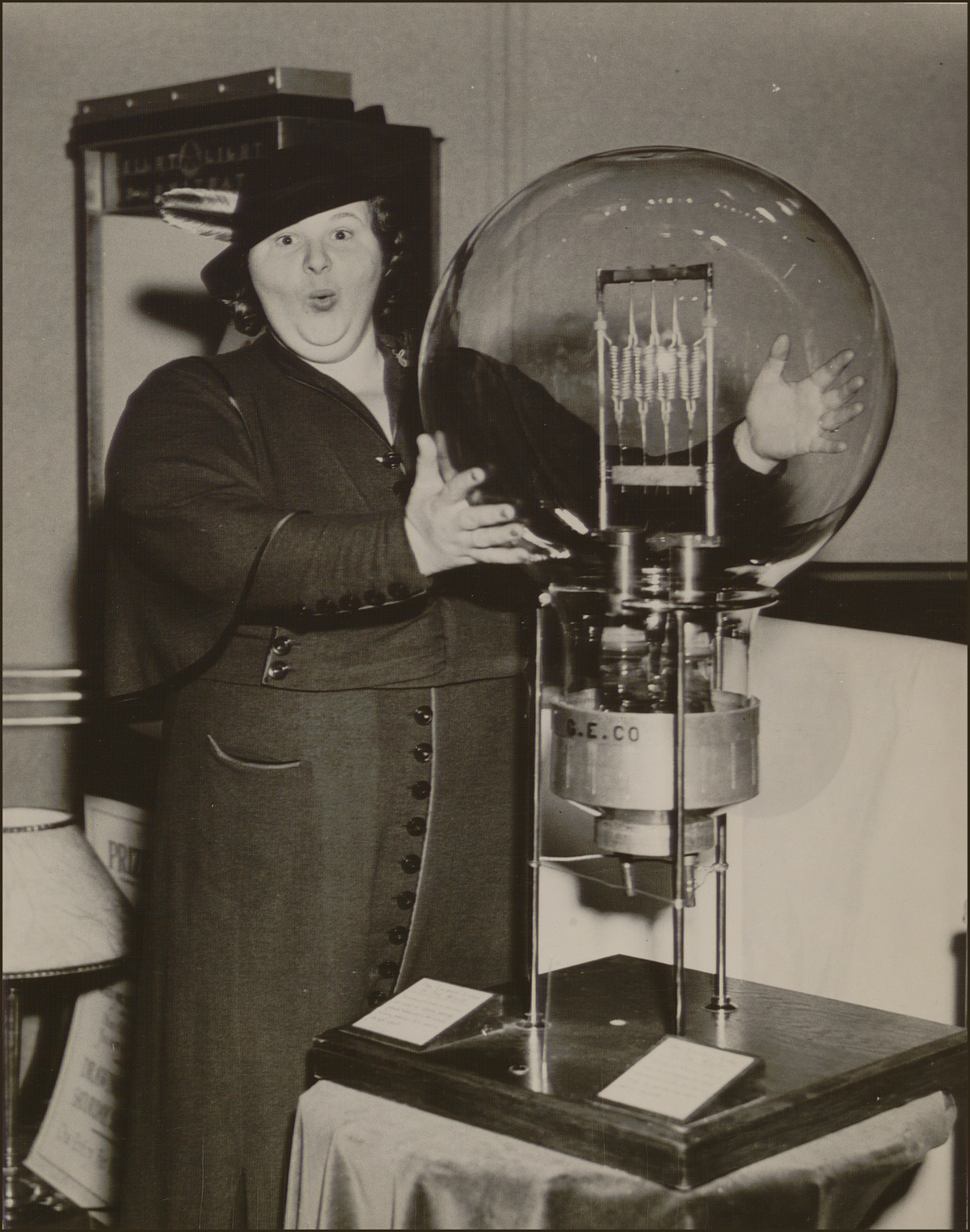 Black and white photo of a woman placing her hands on a very large incandescent light bulb.