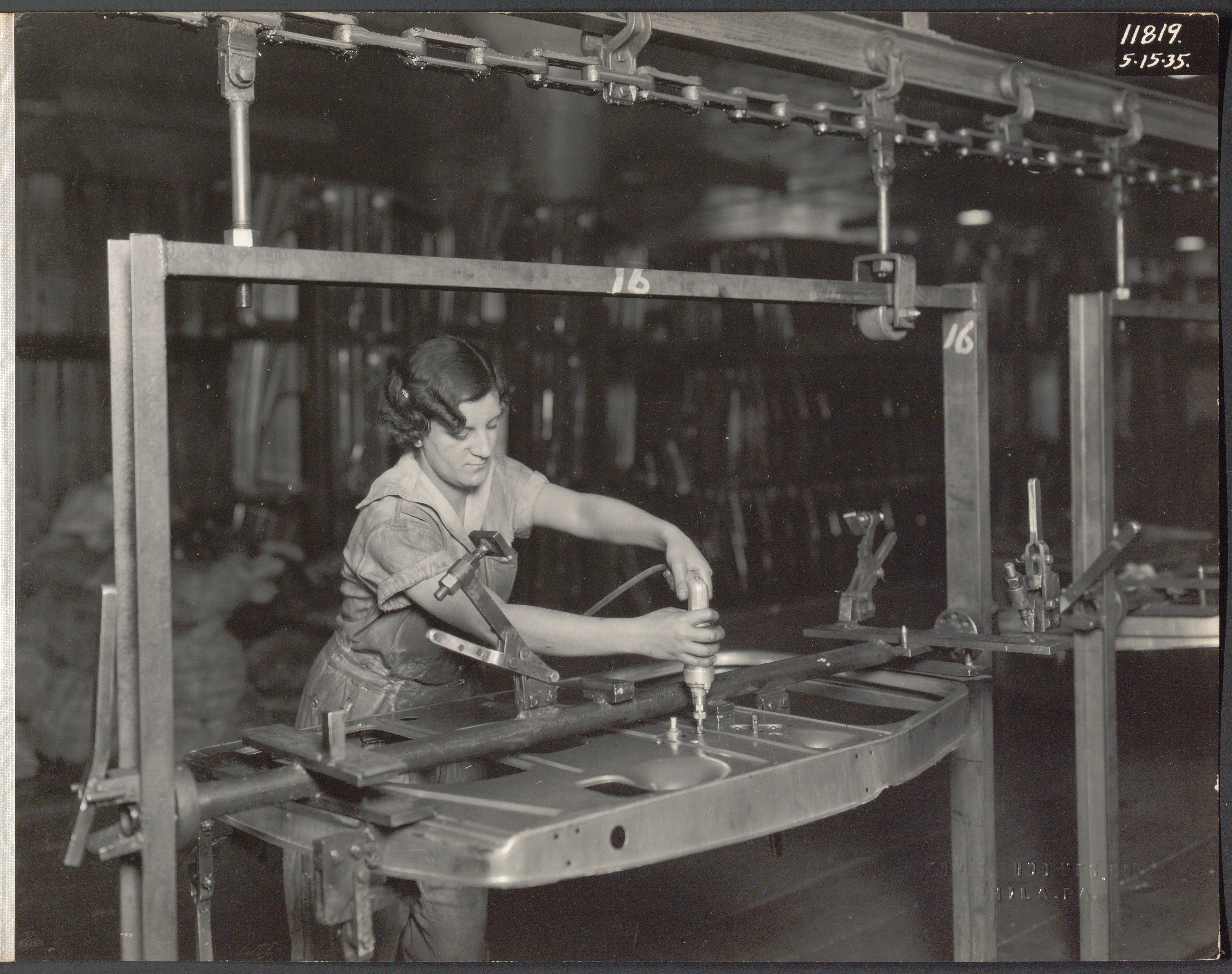 Black and white photograph of a woman in overalls applying fasteners to a metal door panel.