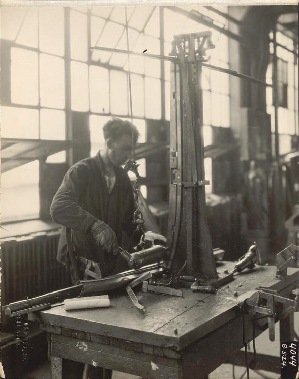 Black and white photograph of a worker in a factory riveting autobody parts.