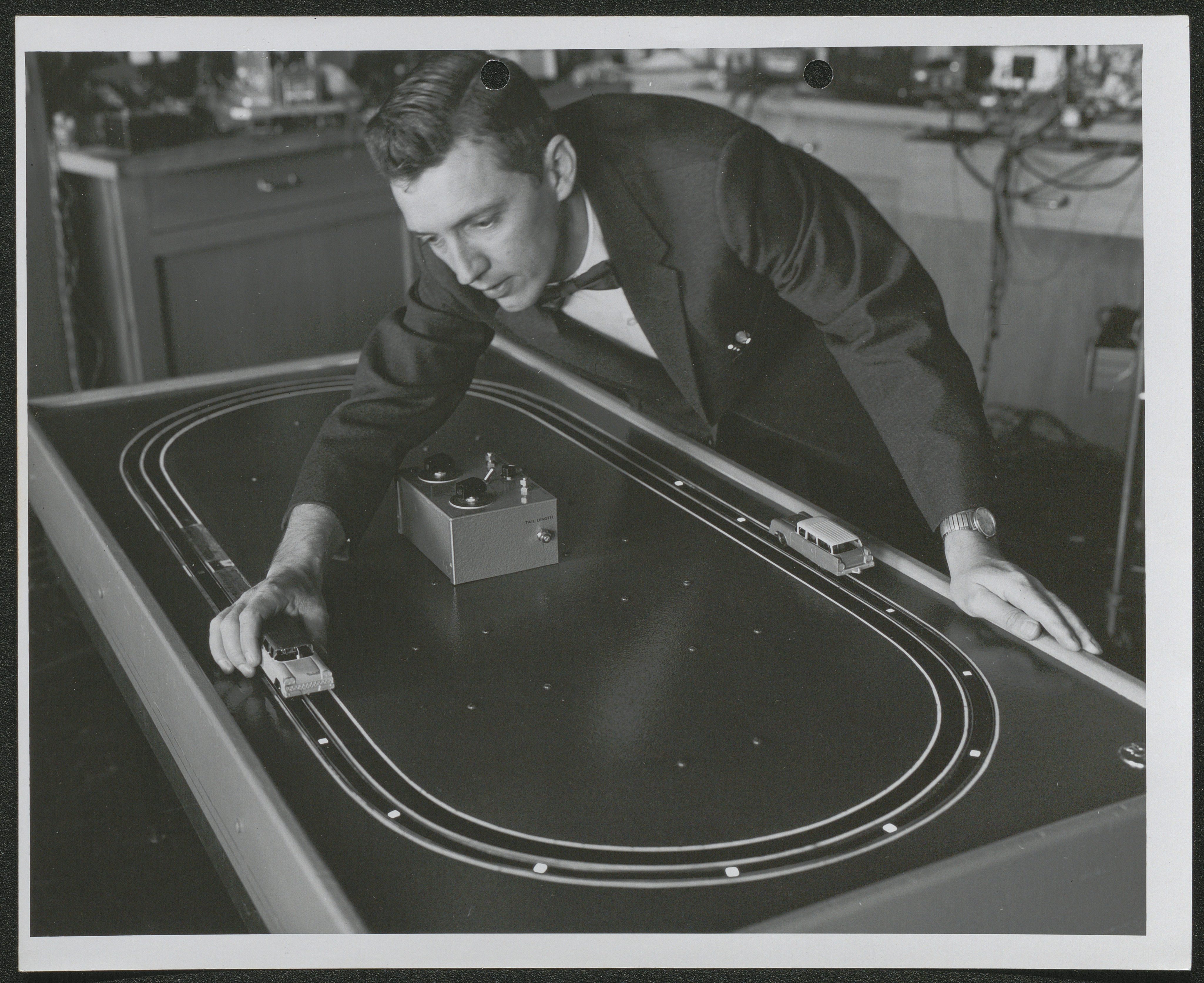 Black and white image of a man moving a model car along an electronic track