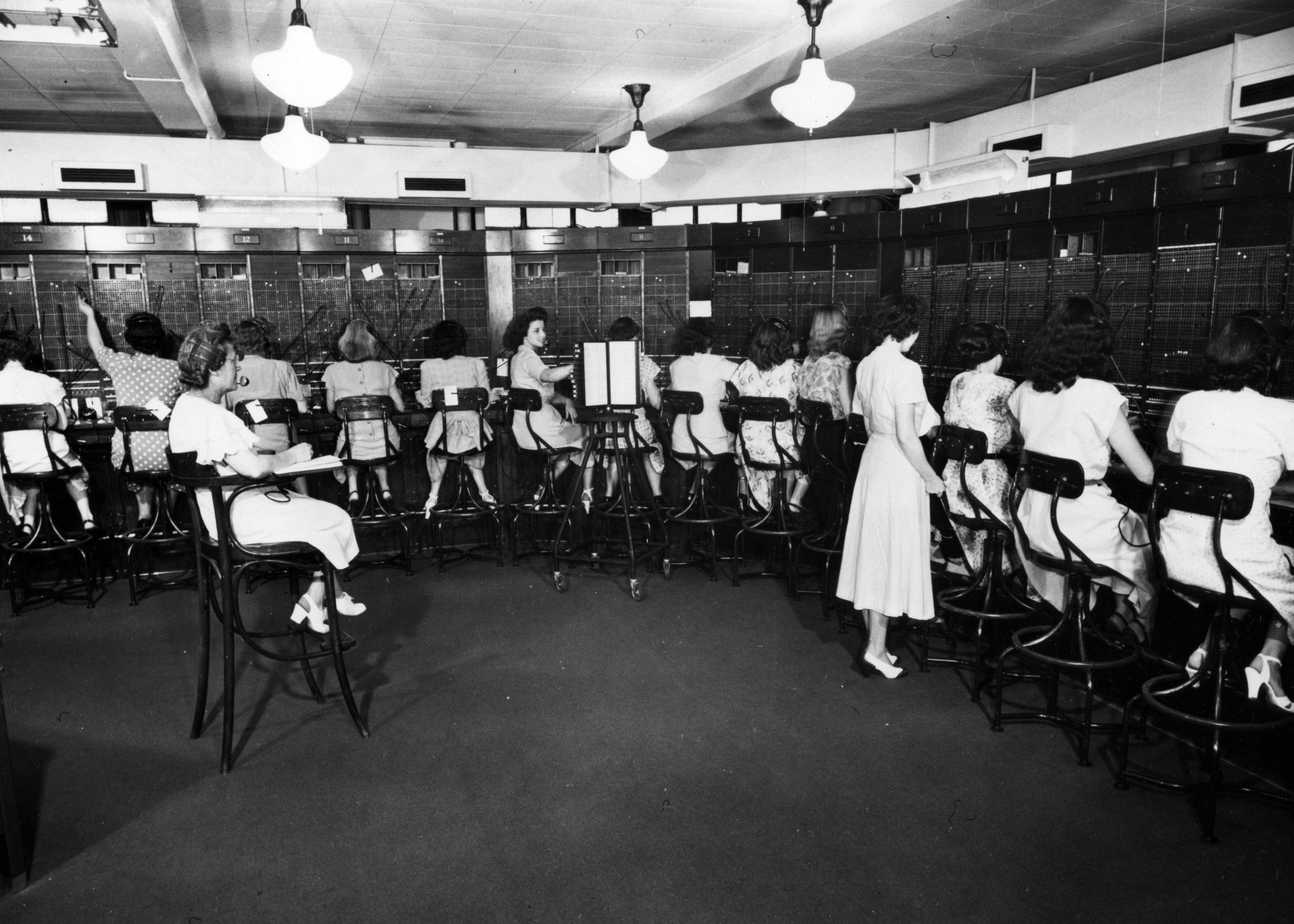Black and white photo of a number of women at work in a large switchboard office.
