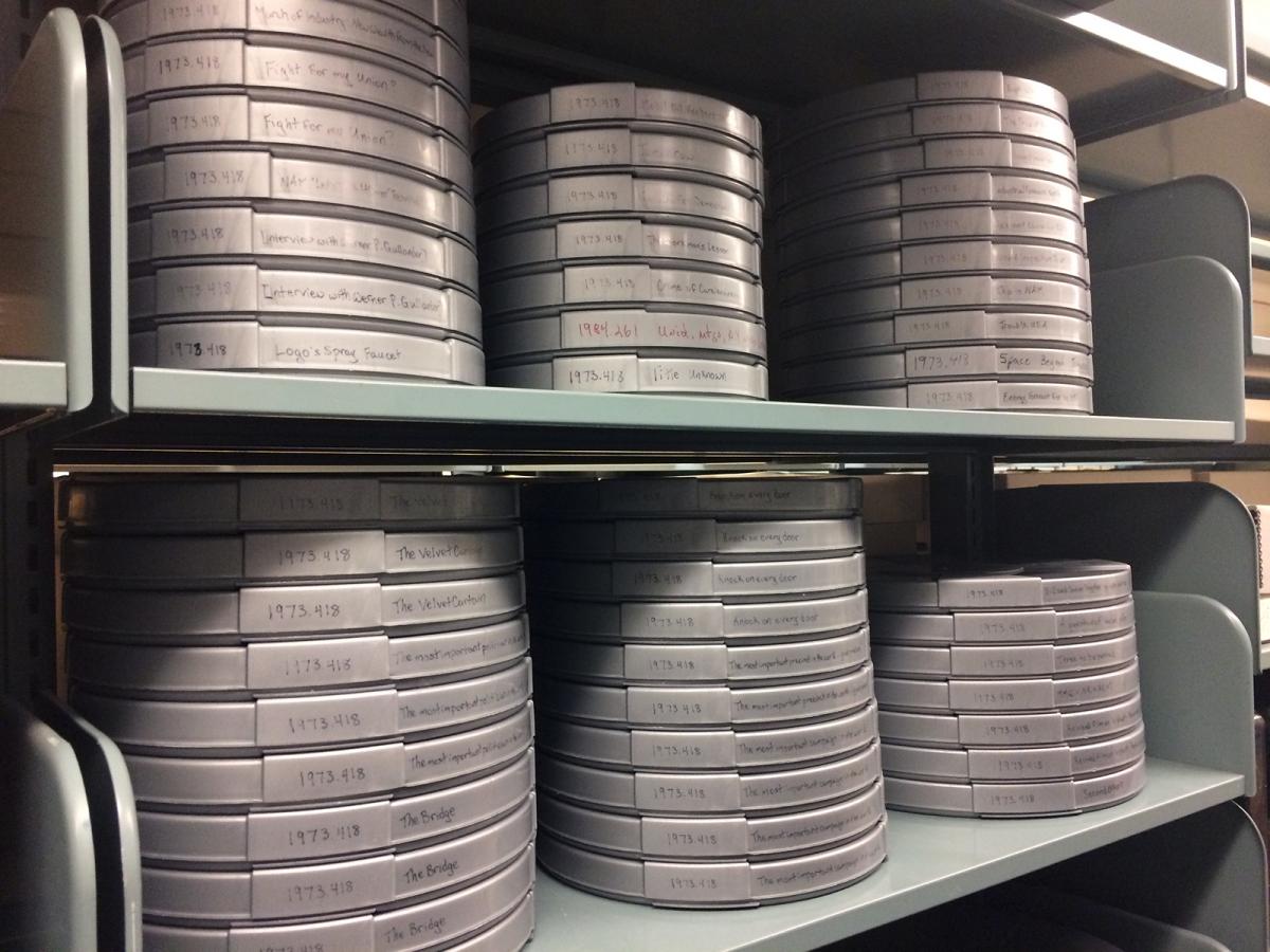 Film reels neatly stacked and labeled on a metal book shelf