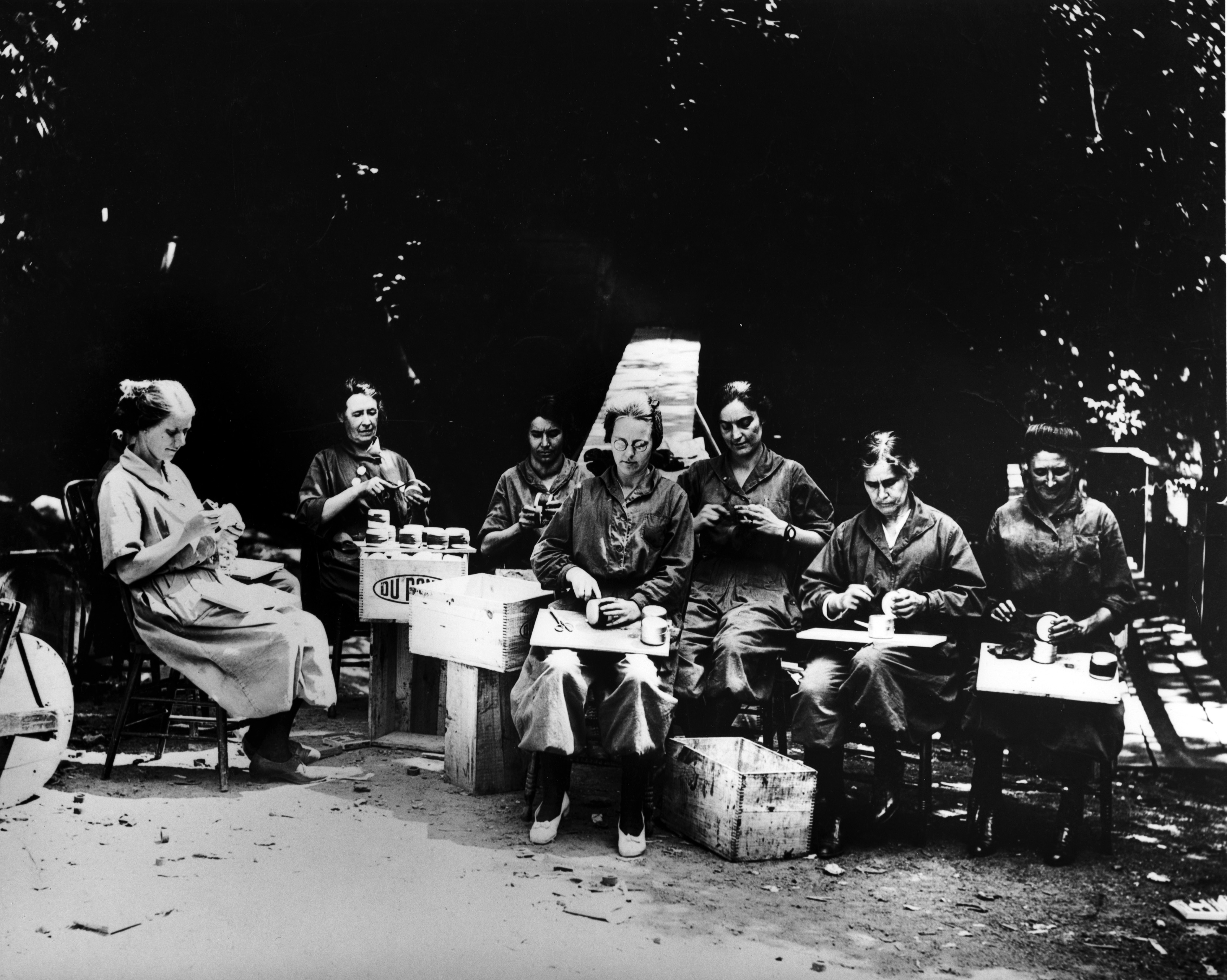 Black and white photograph of a group of seated women  taping and sealing tin containers for rings for 3-inch Stokes Trench Mortar at DuPont Co. Brandywine Mills