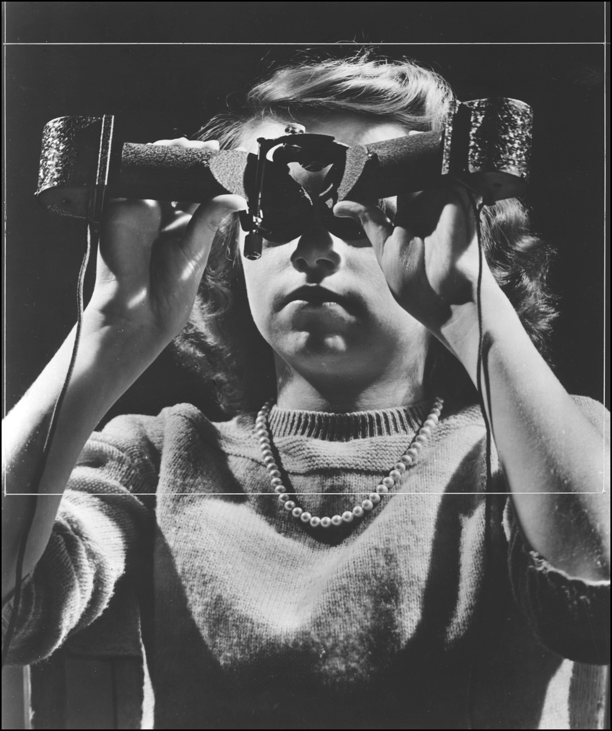 Black and white image of a young woman holding a strange object up to her eyes.