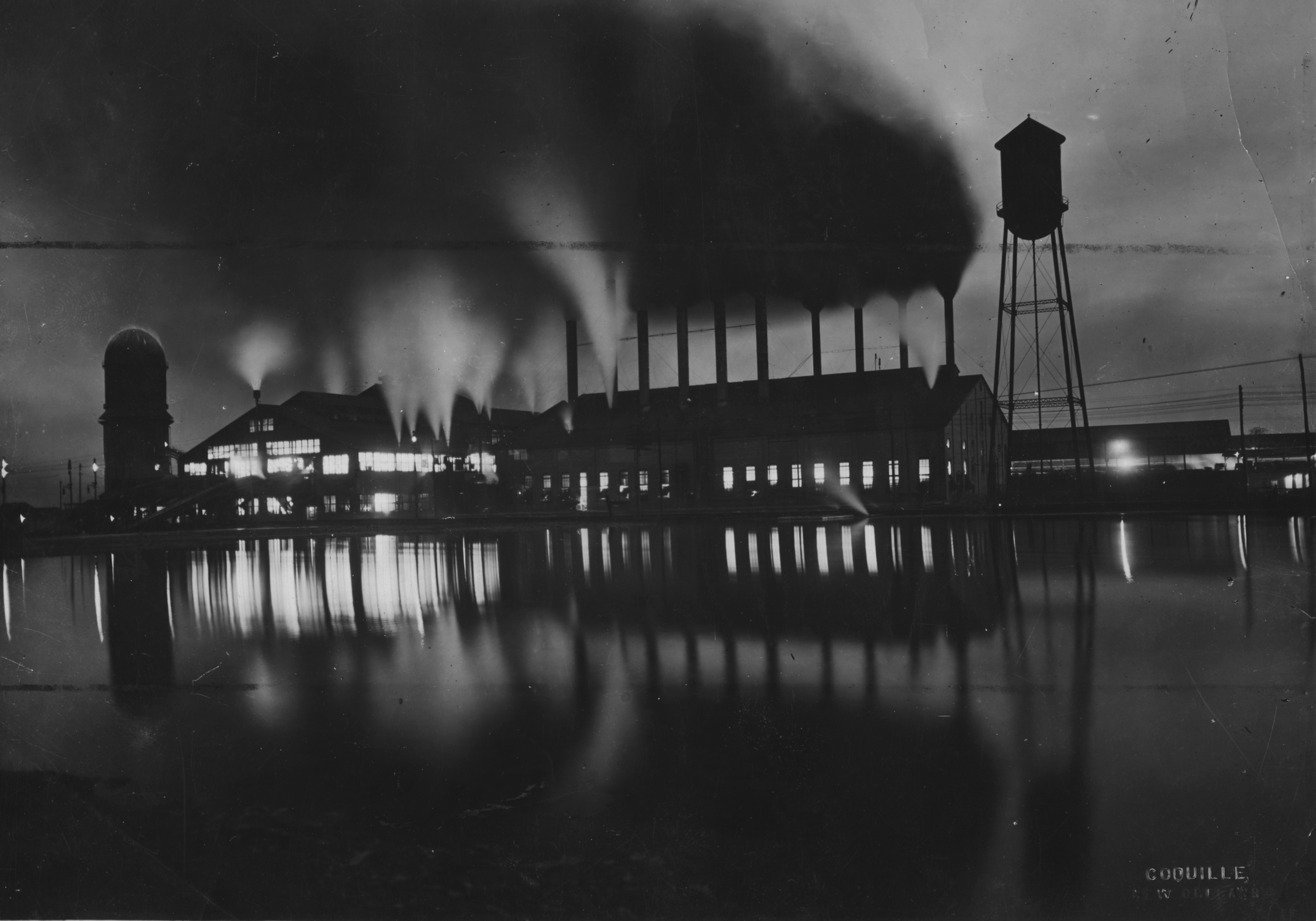 Dramatically lit black and white exterior image of a pine mill in operation at night.