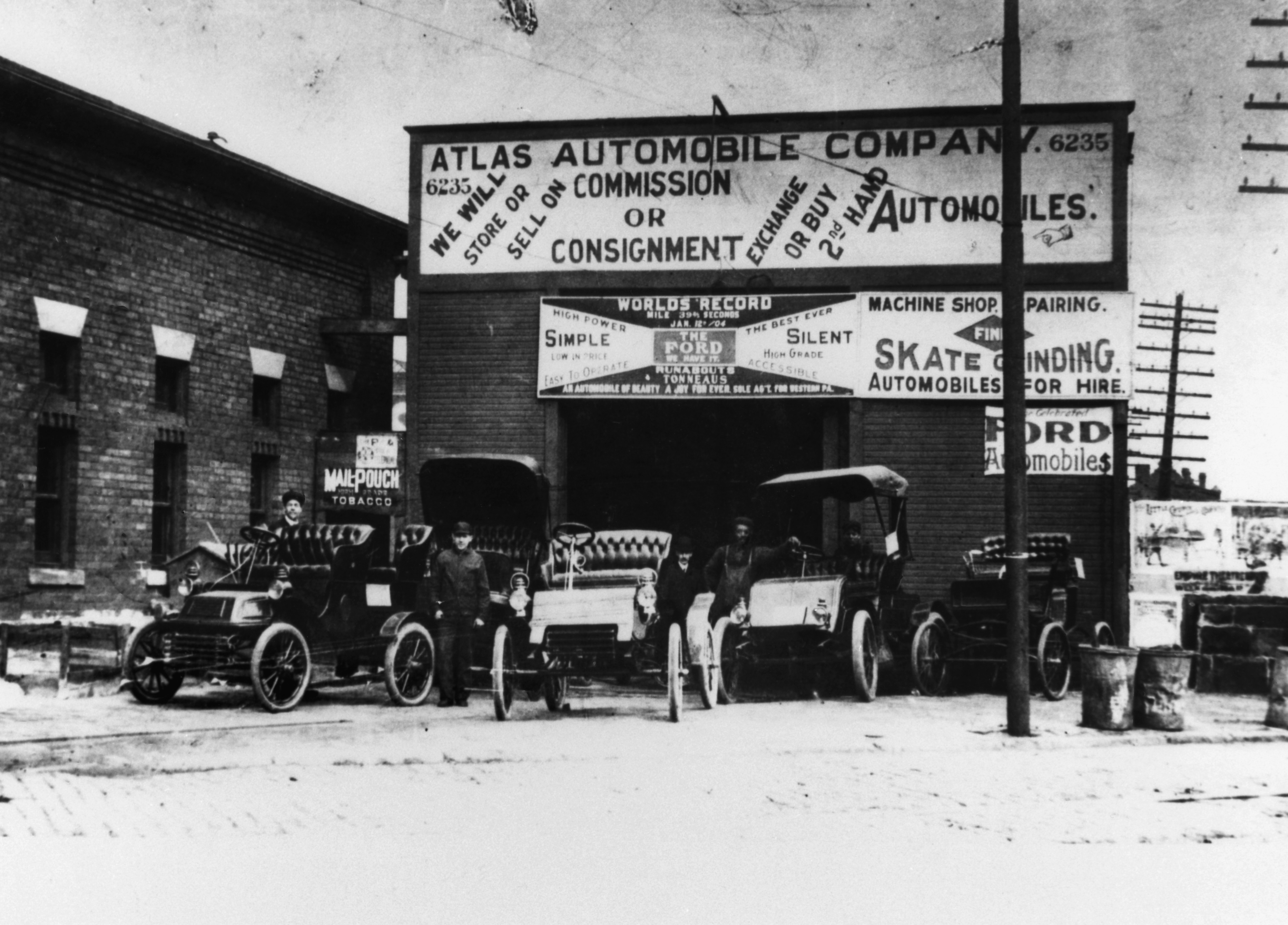 Black and white photograph of cars and staff outside of an early 20th century automobile dealership and service station.