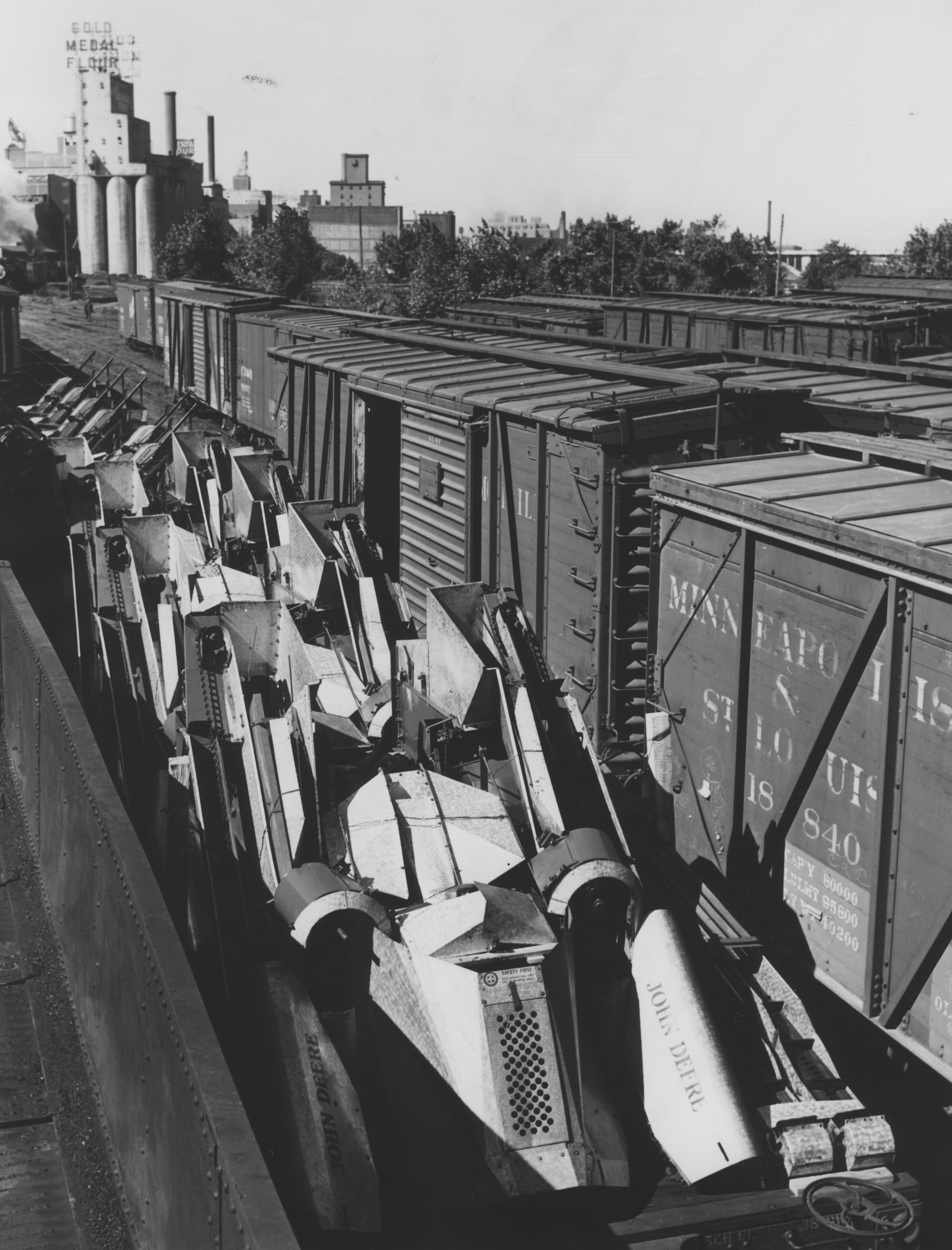 Black and white photograph of John Deere corn shuckers loaded on freight cars 