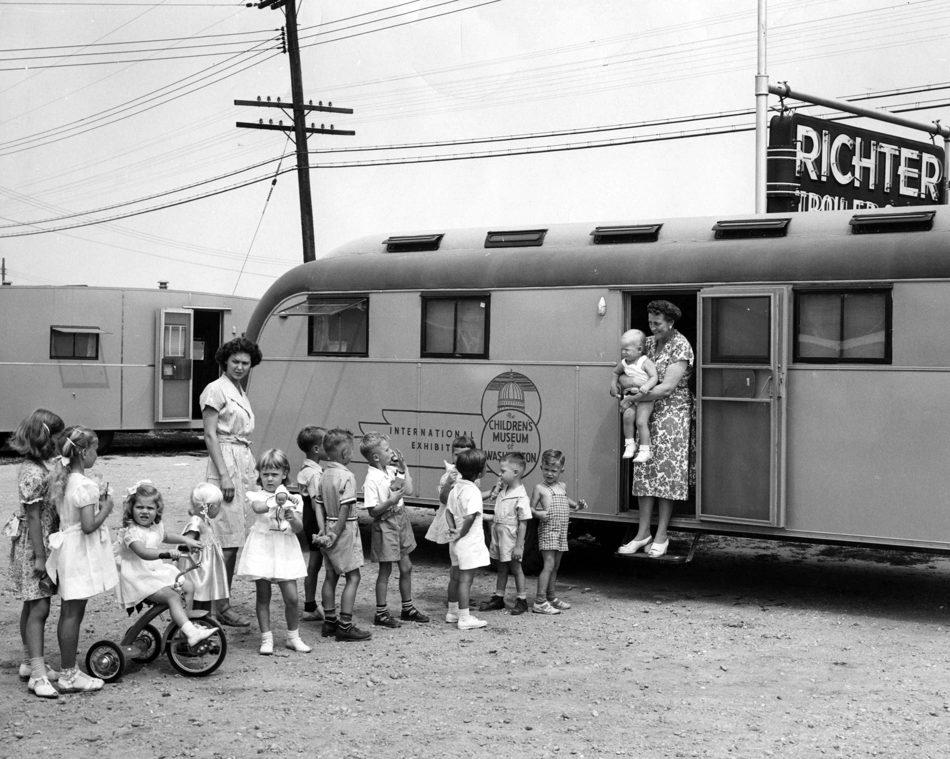 Black and white photograph of children lined up outside a trailer with a traveling museum exhbiit.